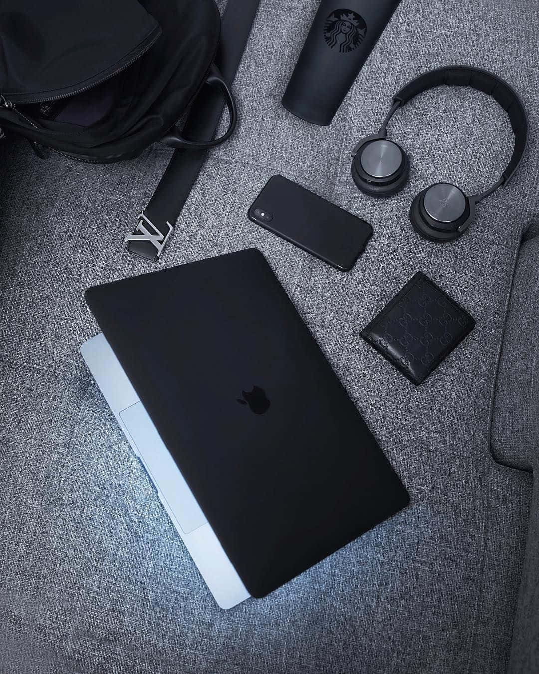 黑色 桌布 壁紙 — 一部時尚的黑色筆記型電腦放在灰色紋理表面上，周圍環繞著現代科技配件和奢侈品。