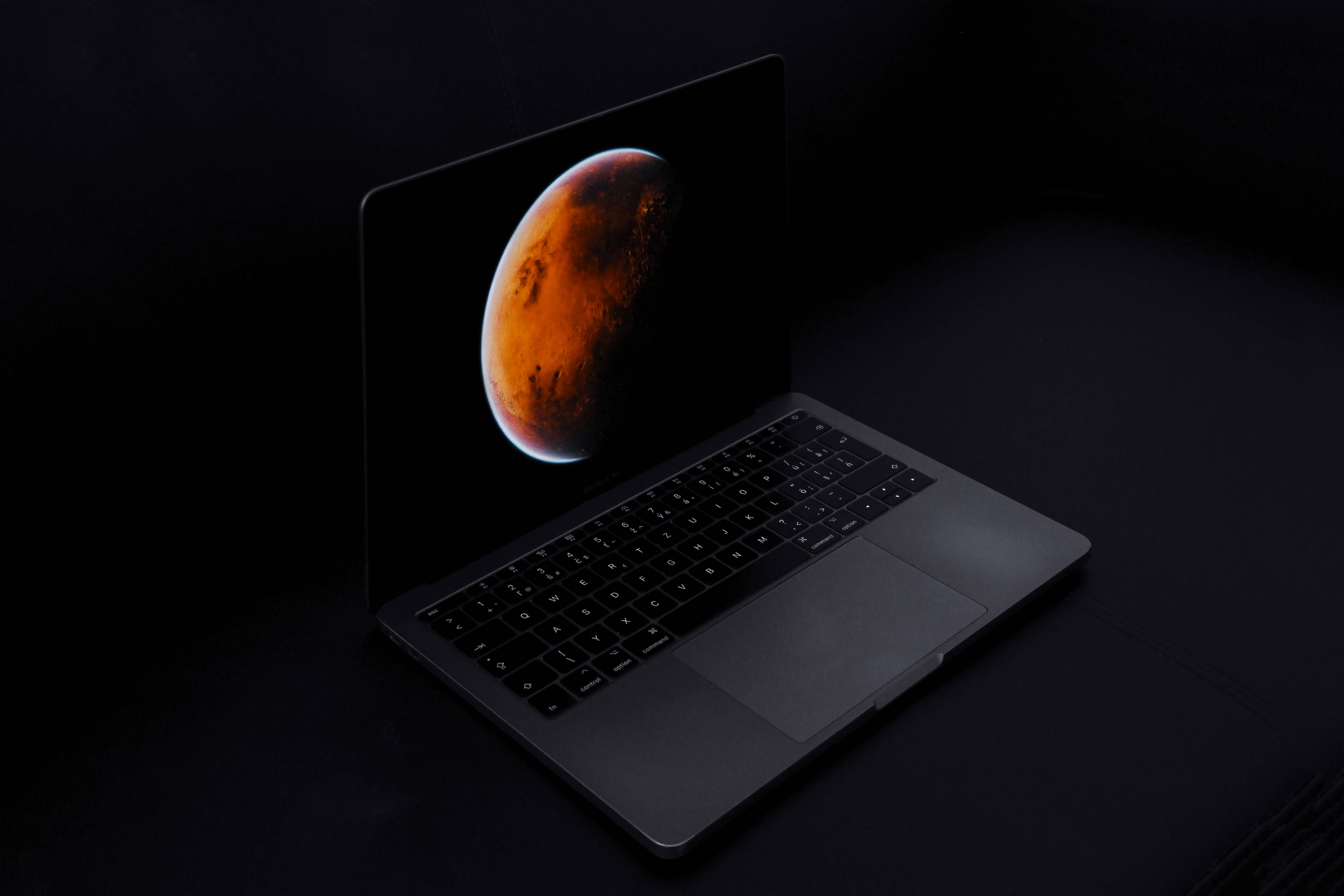 Mac Os 桌布 壁紙 — 一部時尚筆記型電腦在黑暗背景上顯示鮮紅色的行星，呈現極簡科技設置。