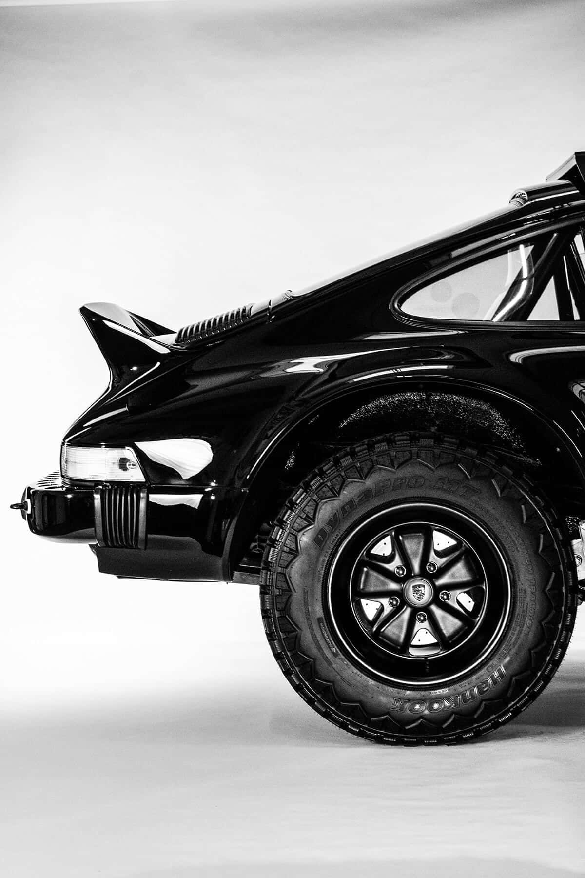 Off-road Car 桌布 壁紙 — 一部時尚黑色改裝保時捷911，配備超大輪胎和後擾流板，在高對比度工作室燈光下拍攝。
