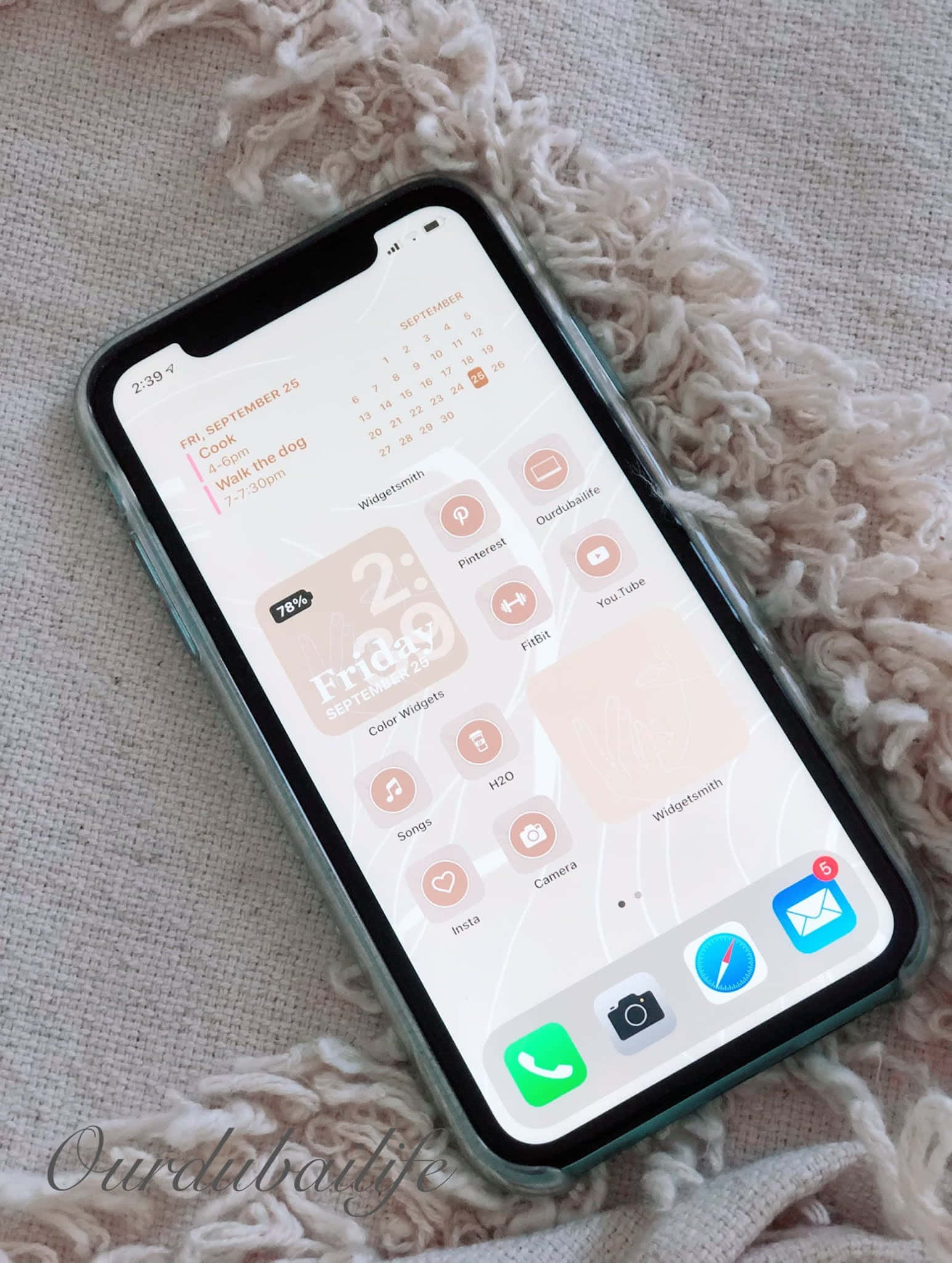 iPhone 美學 桌布 壁紙 — 一部智慧型手機，其主螢幕為粉彩粉紅和蜜桃色，充滿小工具，放在柔軟的質感米色毯子上。