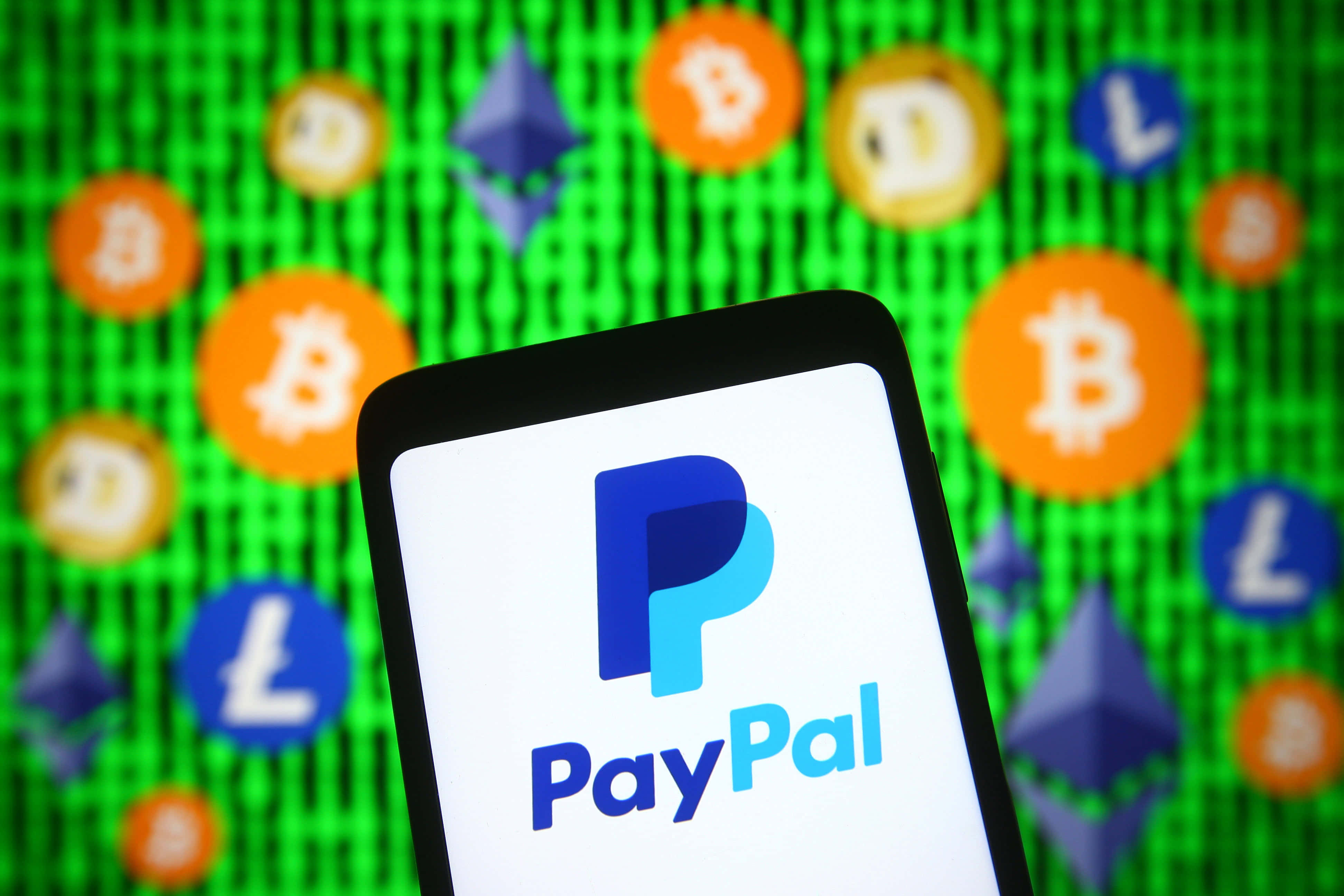 PayPal 桌布 壁紙 — 一部智慧型手機在充滿模糊加密貨幣圖示的綠色螢幕前顯示PayPal標誌。