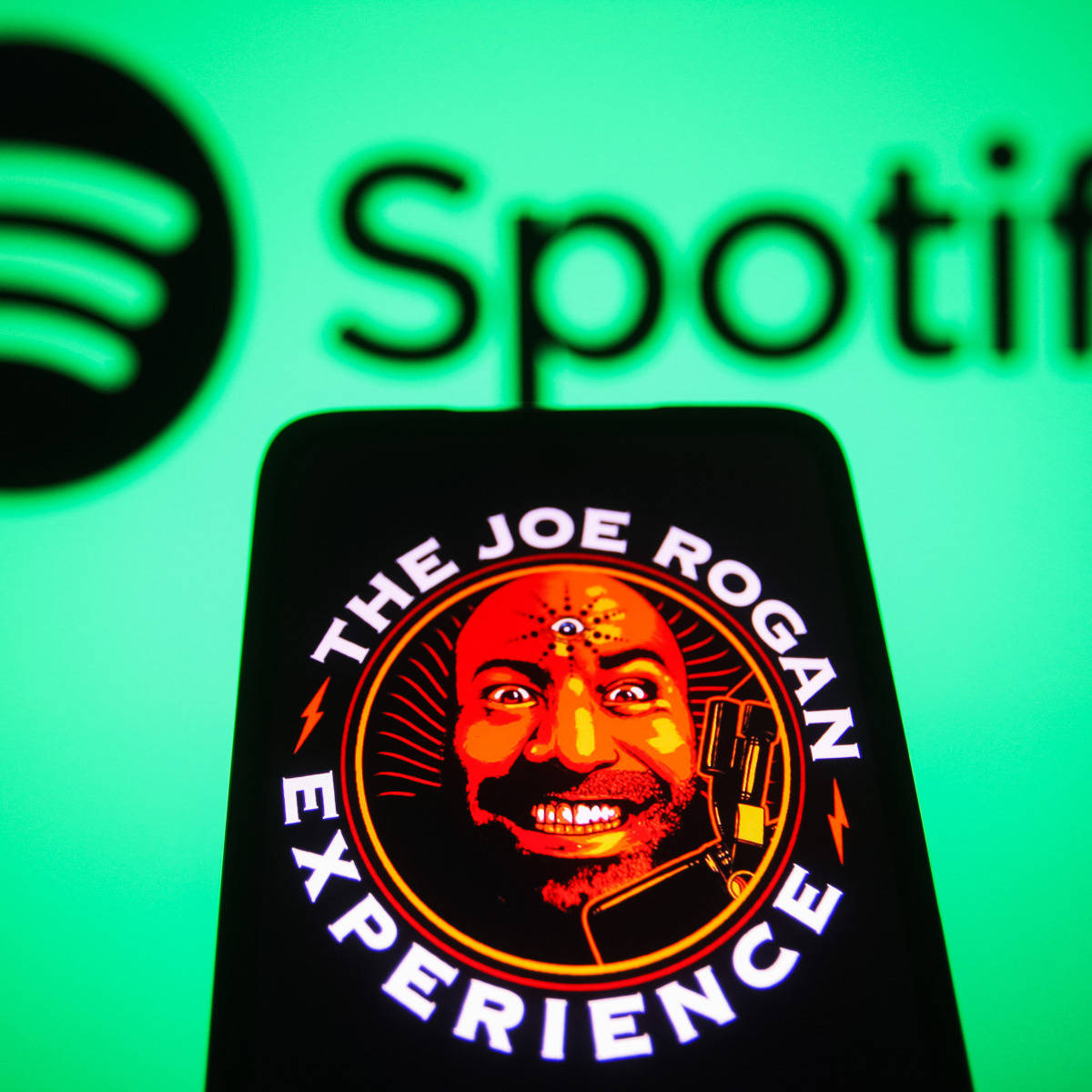 標誌 桌布 壁紙 — 一部智慧型手機在發光的綠色Spotify背景上顯示The Joe Rogan Experience播客標誌。
