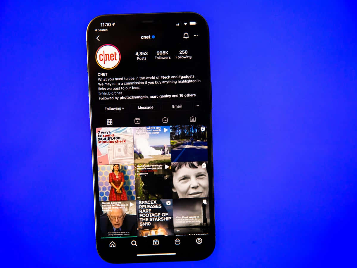 Instagram 桌布 壁紙 — 一部智慧型手機在純藍色背景上顯示CNET Instagram個人資料，並帶有科技和新聞帖子的網格。