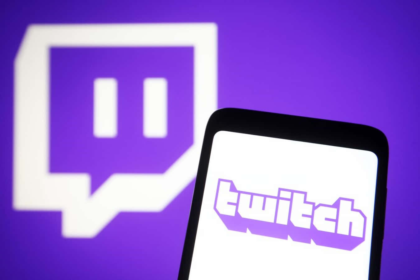 Twitch 桌布 壁紙 — 一部智慧型手機在紫色背景上顯示 Twitch 標誌，背後有一個大的模糊 Twitch 標誌。