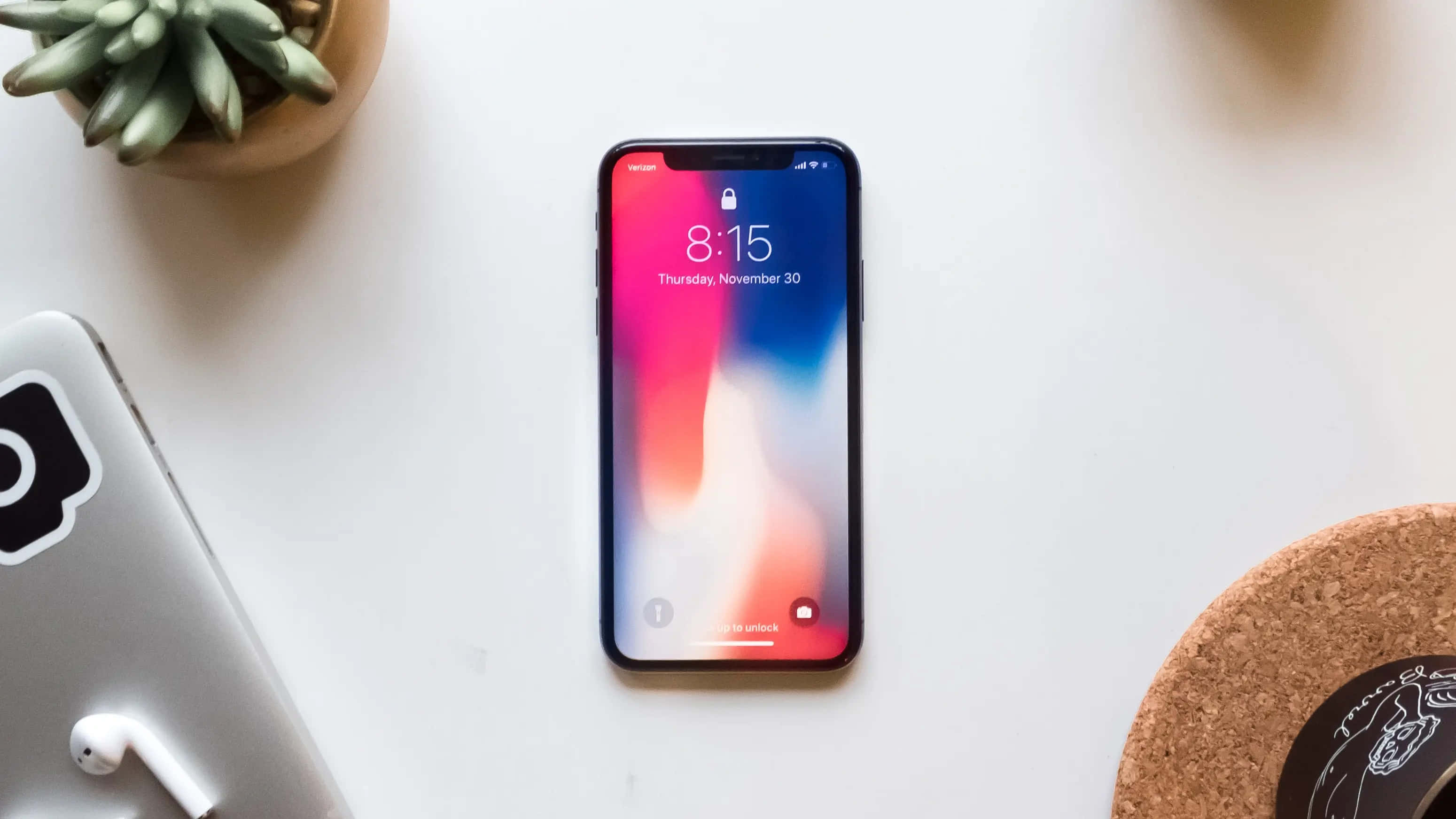 Cool Design iPhone 桌布 壁紙 — 一部智慧型手機帶有彩色漸層桌布，放在白色書桌中央，旁邊有一盆多肉植物和耳塞。