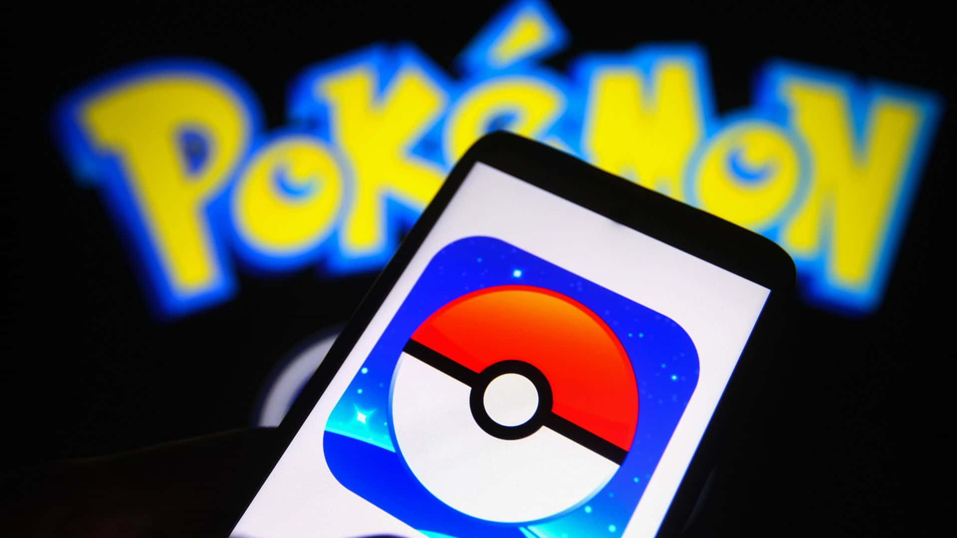 Pokemon Virtual World 桌布 壁紙 — 一部智慧型手機顯示 Pokémon 應用程式圖示，背景中發光的 Pokémon 標誌模糊不清。