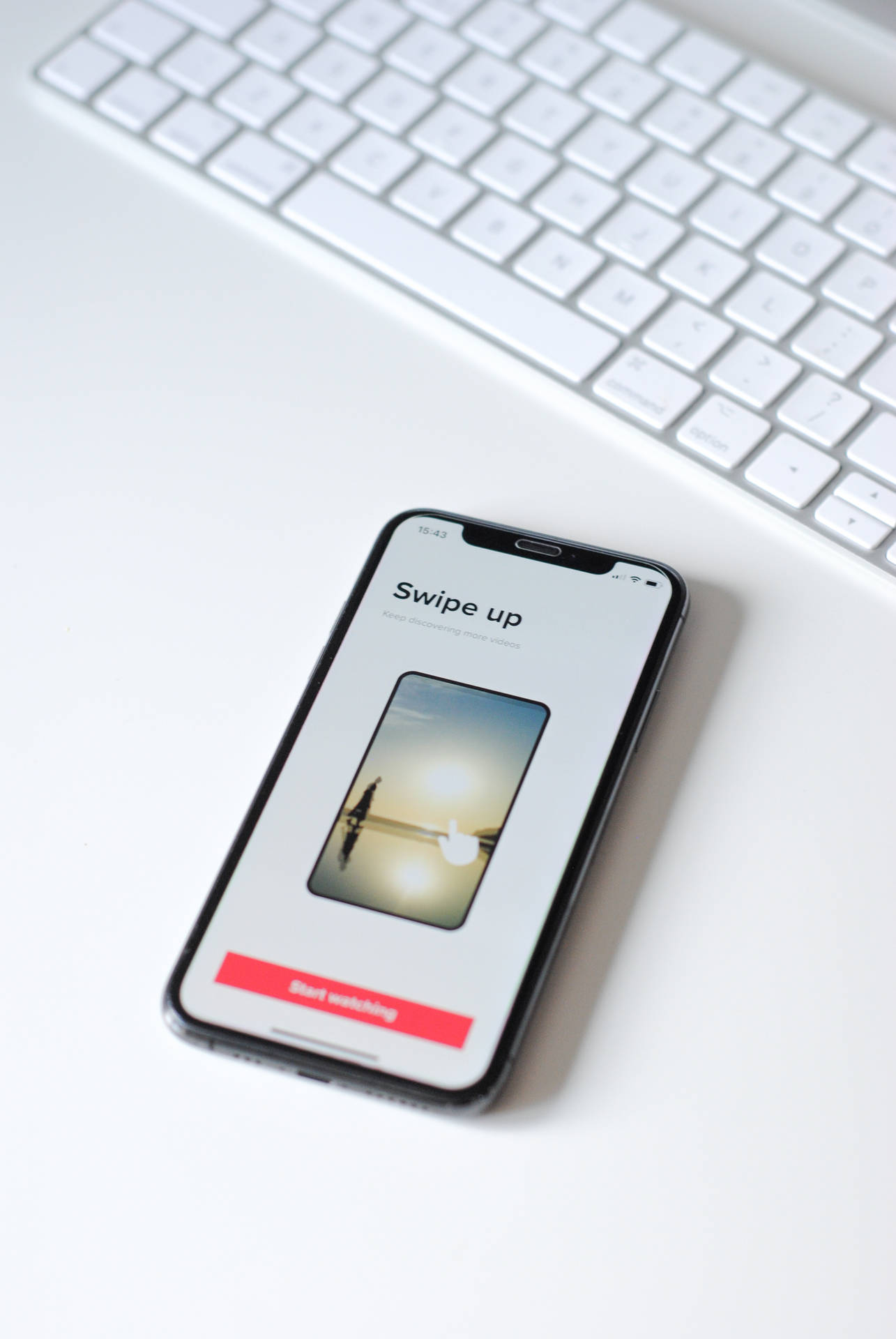 白色桌子上鍵盤旁的智慧型手機顯示向上滑動應用程式 — 頂級 iPhone 桌布 壁紙