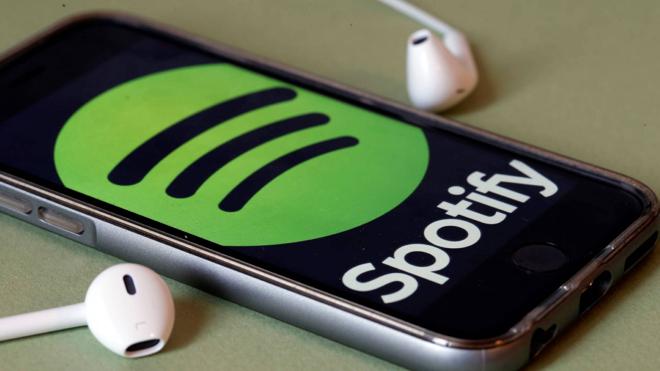 Spotify 桌布 壁紙 — 一部智慧型手機顯示Spotify標誌，白色耳機放在旁邊的柔和綠色表面上。