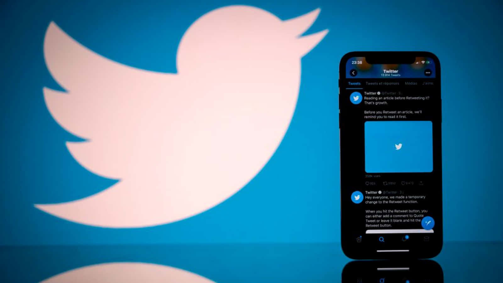 Twitter 桌布 壁紙 — 一部智慧型手機顯示Twitter應用程式介面，站在藍色背景前一個大型發光的Twitter鳥標誌前。