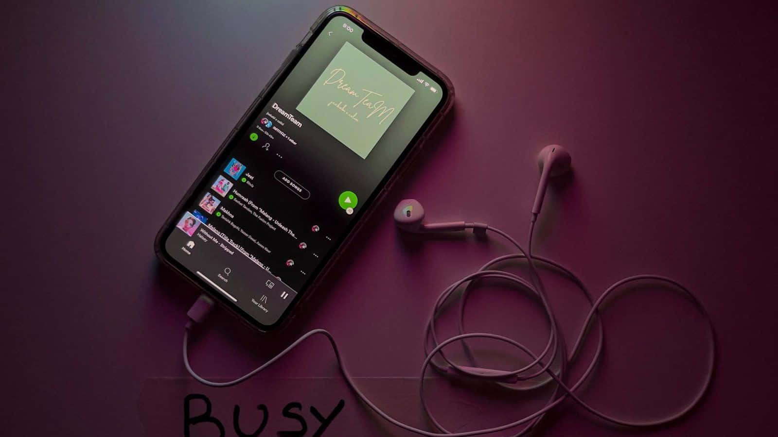 iPhone 桌布 壁紙 — 一部智慧型手機顯示音樂應用程式，耳機纏繞在附近，放在深紫色表面上，下方寫有「BUSY」字樣。