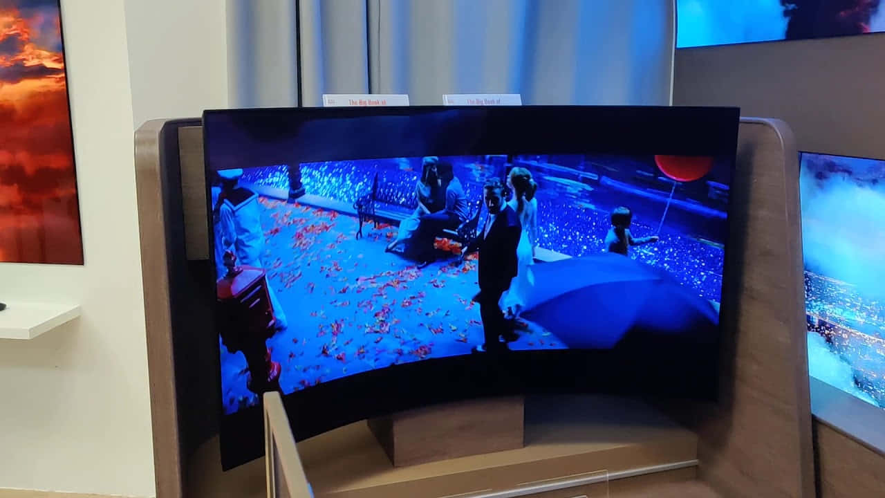 科技動圖 桌布 壁紙 — 一部曲面電視顯示藍色調的場景，一對情侶在夜間撐著傘，周圍有紅色花瓣飄落。