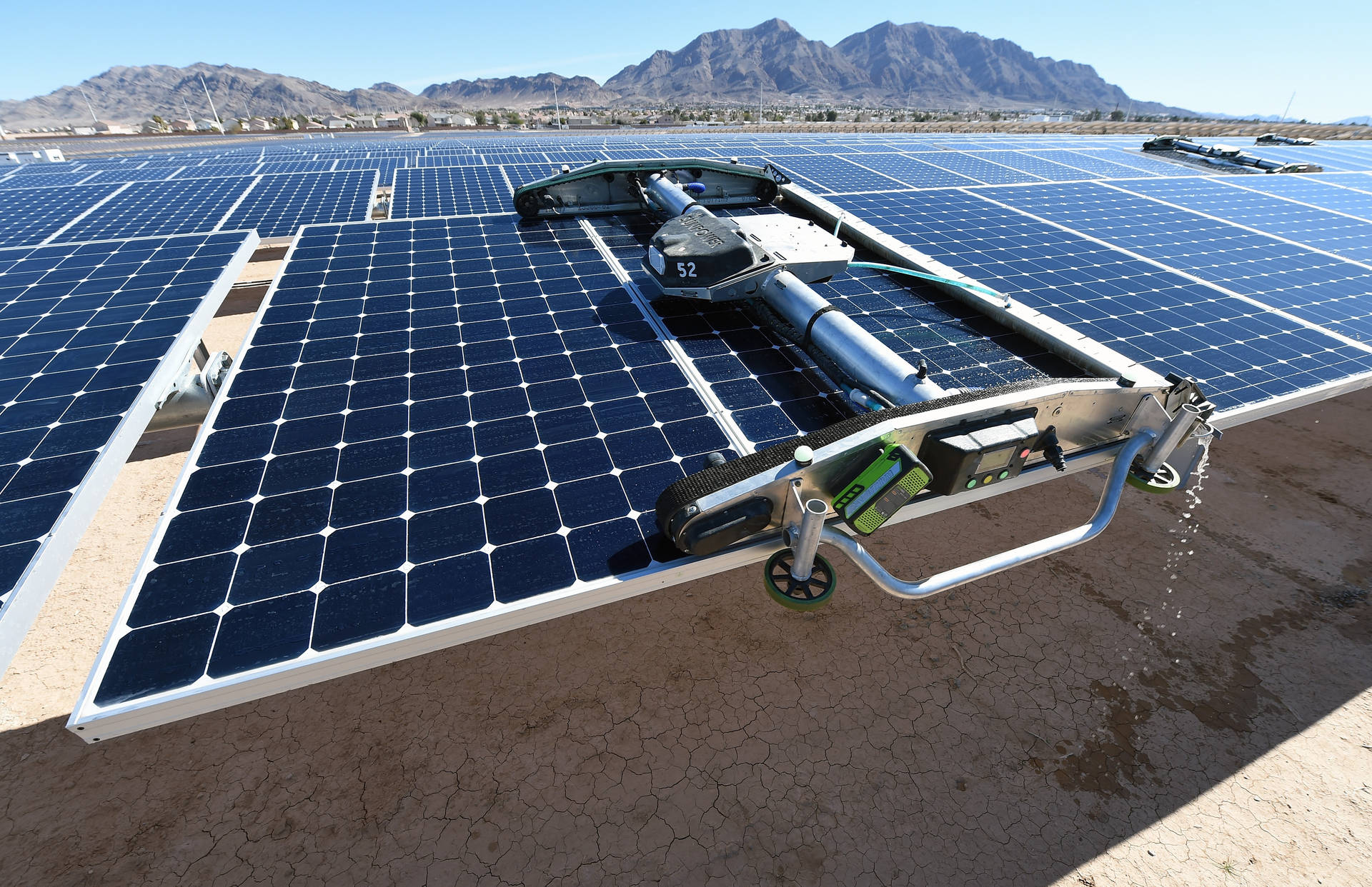 科技動圖 桌布 壁紙 — 一部機器人清潔機在晴朗藍天下清洗太陽能板，背景有遠山。