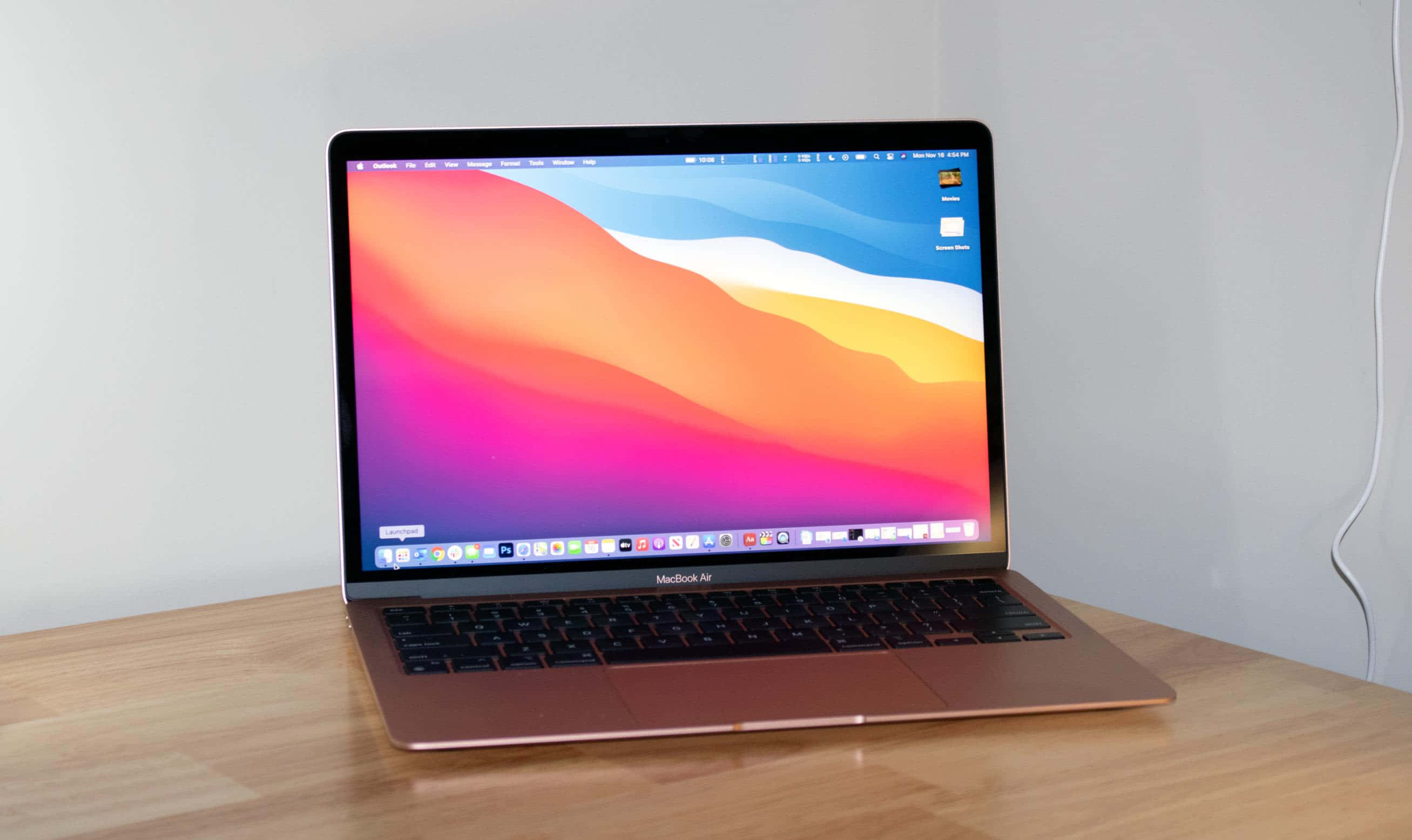 MacBook 動態圖片 桌布 壁紙 — 一部玫瑰金色 MacBook Air 打開放在木桌上，顯示一幅充滿活力的抽象桌布，帶有粉紅、橙色和藍色的流動漸變。