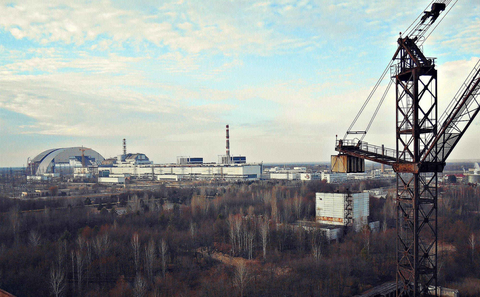 風景 桌布 壁紙 — 一部生鏽的起重機佔據前景，俯瞰著車諾比核電廠及其獨特的圓頂，天空部分多雲。