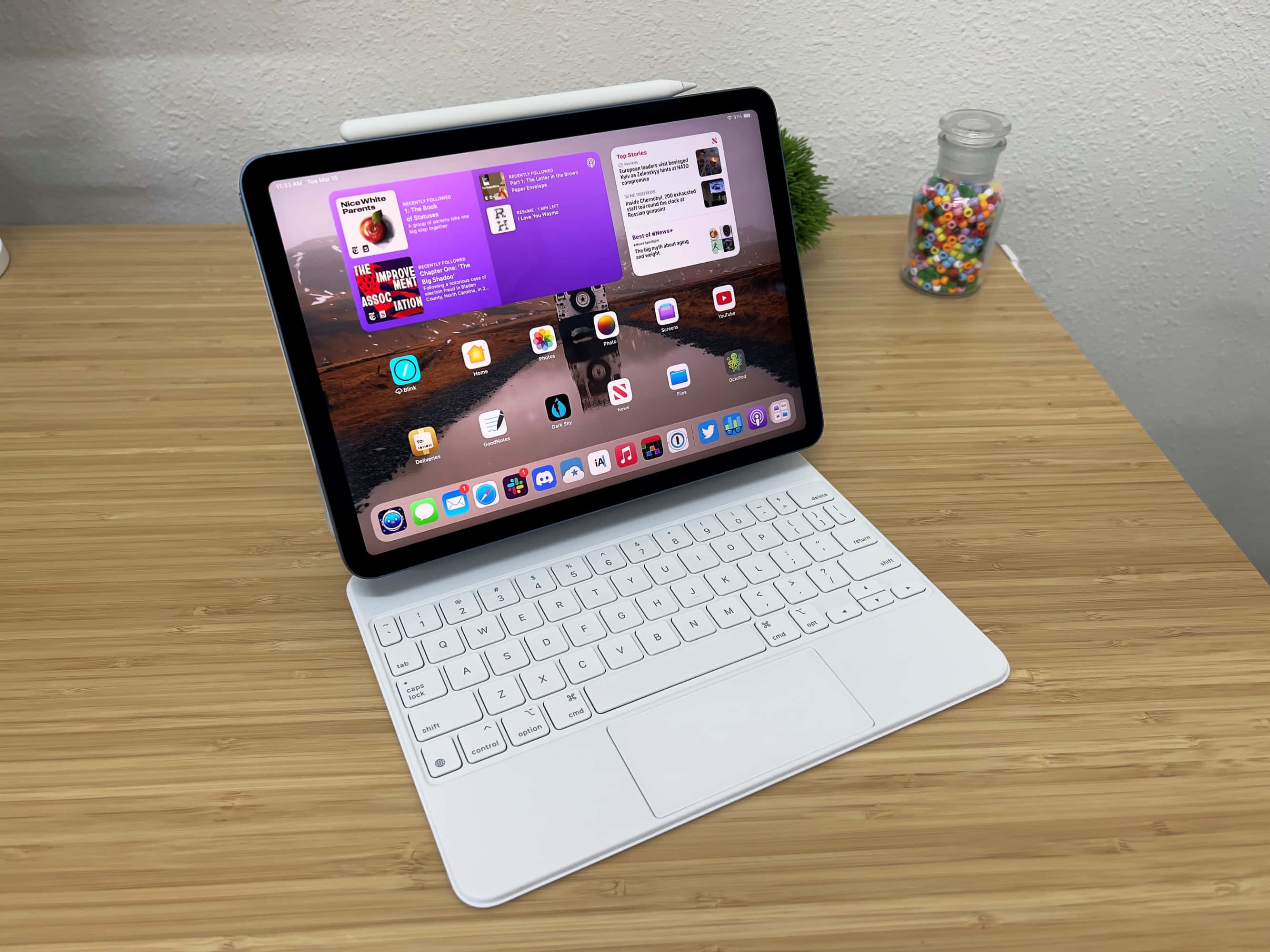 iPad 桌布 壁紙 — 一部白色iPad連鍵盤保護套放在木桌上，顯示鮮豔的紫色桌布和應用程式圖示。