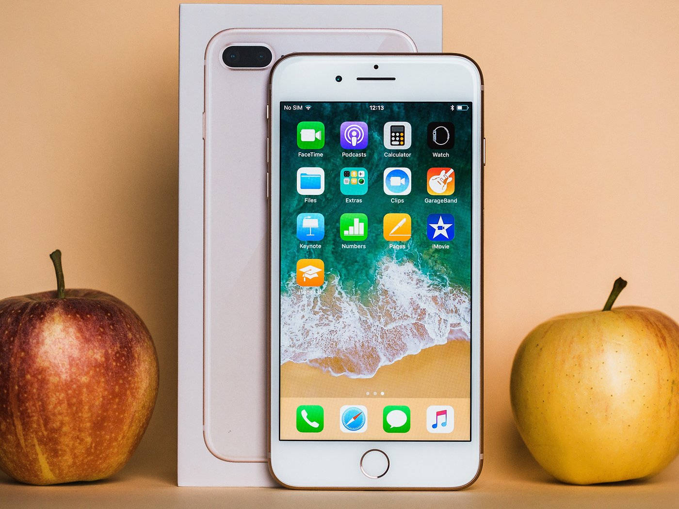 iPhone 8 桌布 壁紙 — 一部白色iPhone 8 Plus直立放在盒子旁邊，兩側有兩個真蘋果，背景是溫暖的米色。