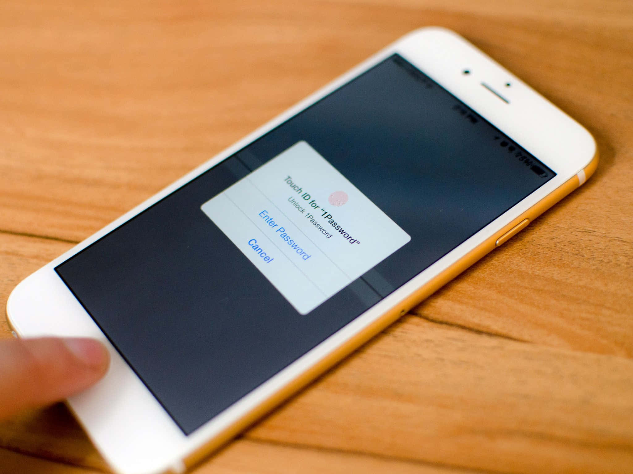 Touch Id 桌布 壁紙 — 一部白色金色邊框的iPhone放在木質表面上，手指懸停在Touch ID感應器上方以解鎖裝置。