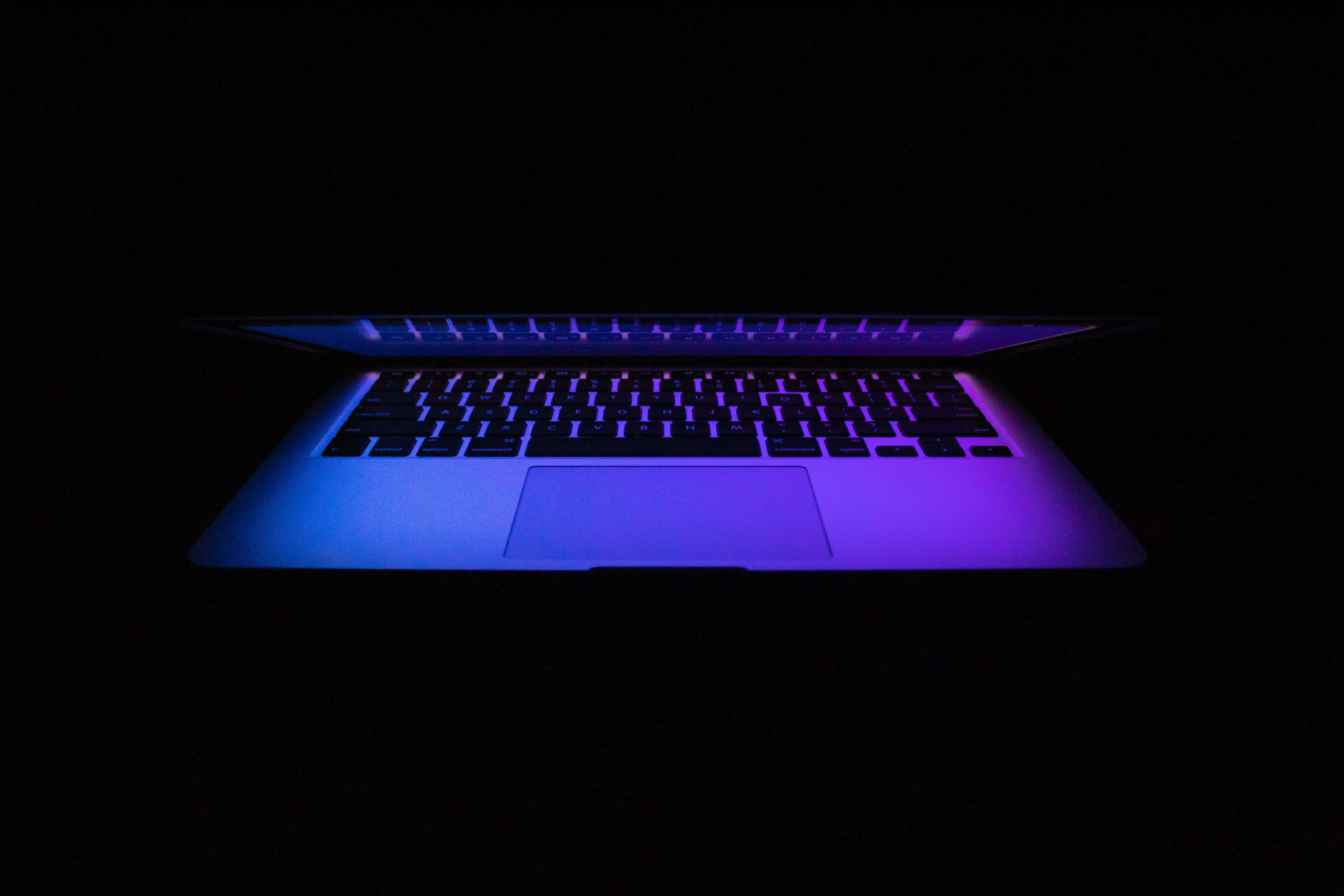 筆電 桌布 壁紙 — 一部筆記型電腦在漆黑的背景下散發出鮮豔的藍色和紫色背光。