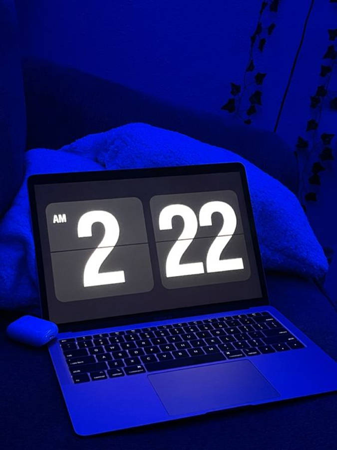 dark blue aesthetic tumblr 桌布 壁紙 — 一部筆記型電腦在黑暗螢幕上以粗體白色數字顯示凌晨2:22，沐浴在柔軟沙發上的冷藍色環境光中。