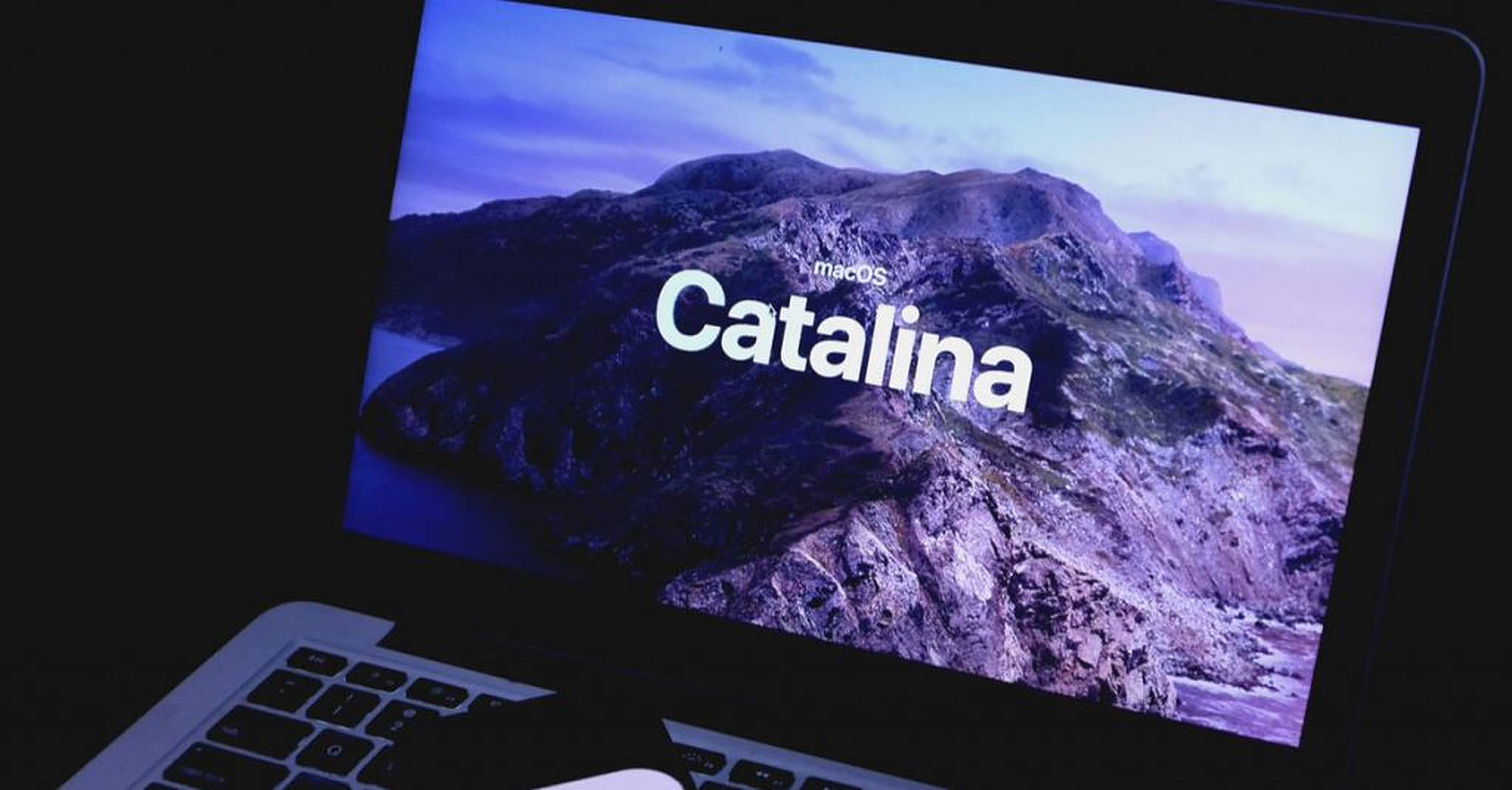 Catalina 桌布 壁紙 — 一部筆記型電腦顯示macOS Catalina的啟動畫面，背景是暮色天空下的紫色山脈景觀。