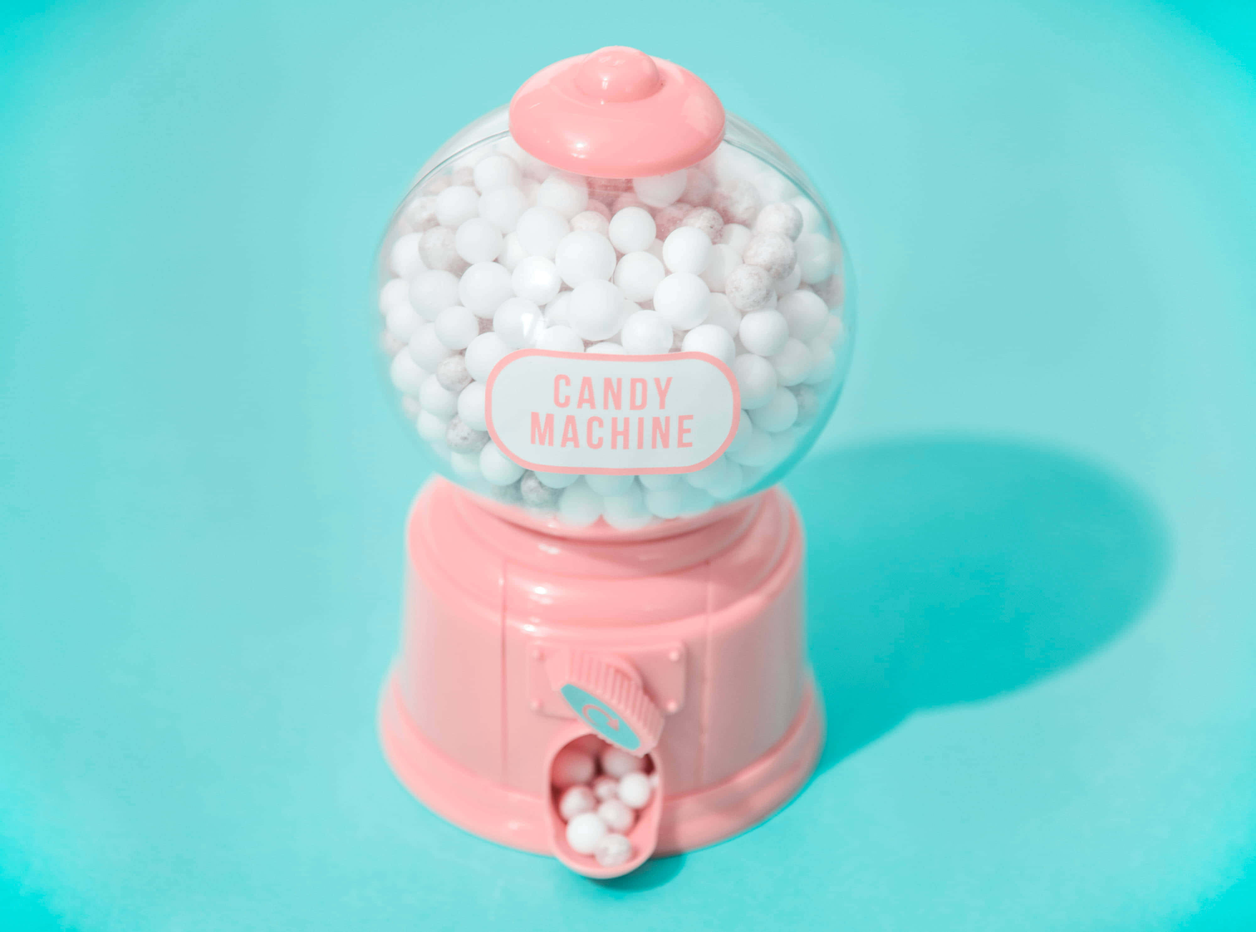 Candy Aesthetic 桌布 壁紙 — 一部粉紅色的口香糖球機裝滿白色球體，放在鮮豔的藍綠色背景前。