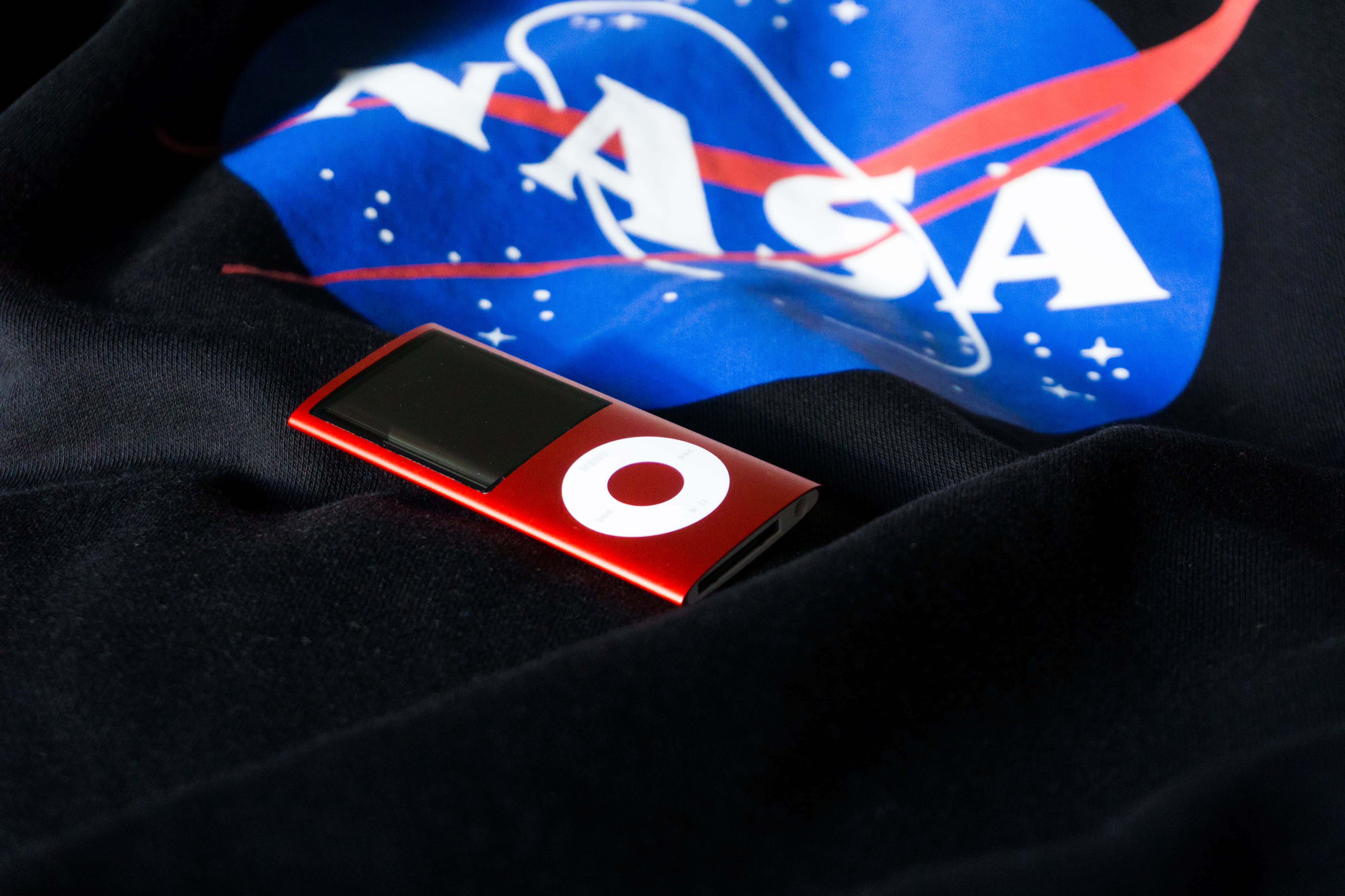 酷炫美學 桌布 壁紙 — 一部紅色 iPod nano 放在一件印有藍、紅、白三色大膽 NASA 標誌的黑色 T 恤上。