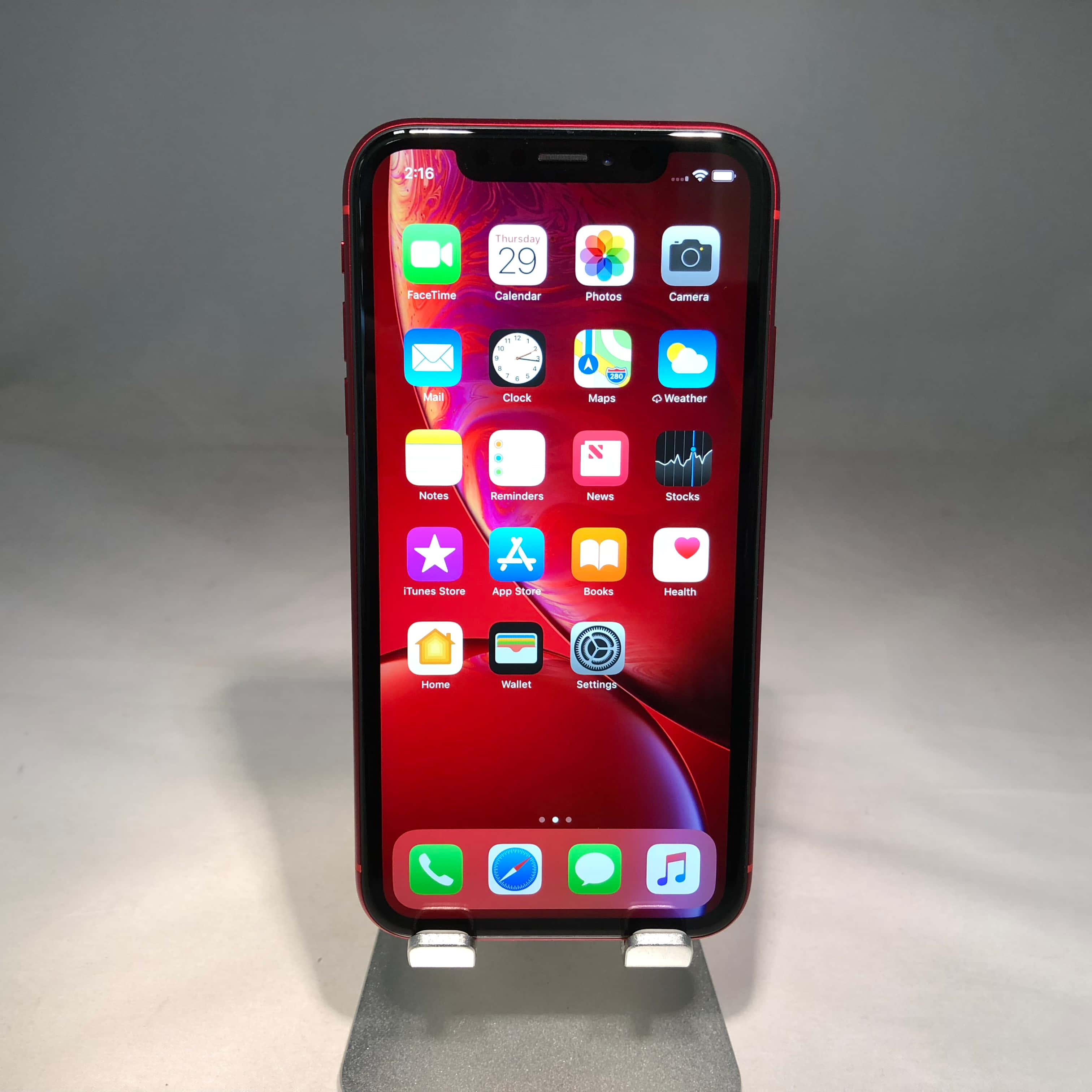 Apple Phone 桌布 壁紙 — 一部紅色iPhone XR直立於支架上，顯示主畫面，色彩繽紛的應用程式圖標襯托著旋轉的紅色桌布。