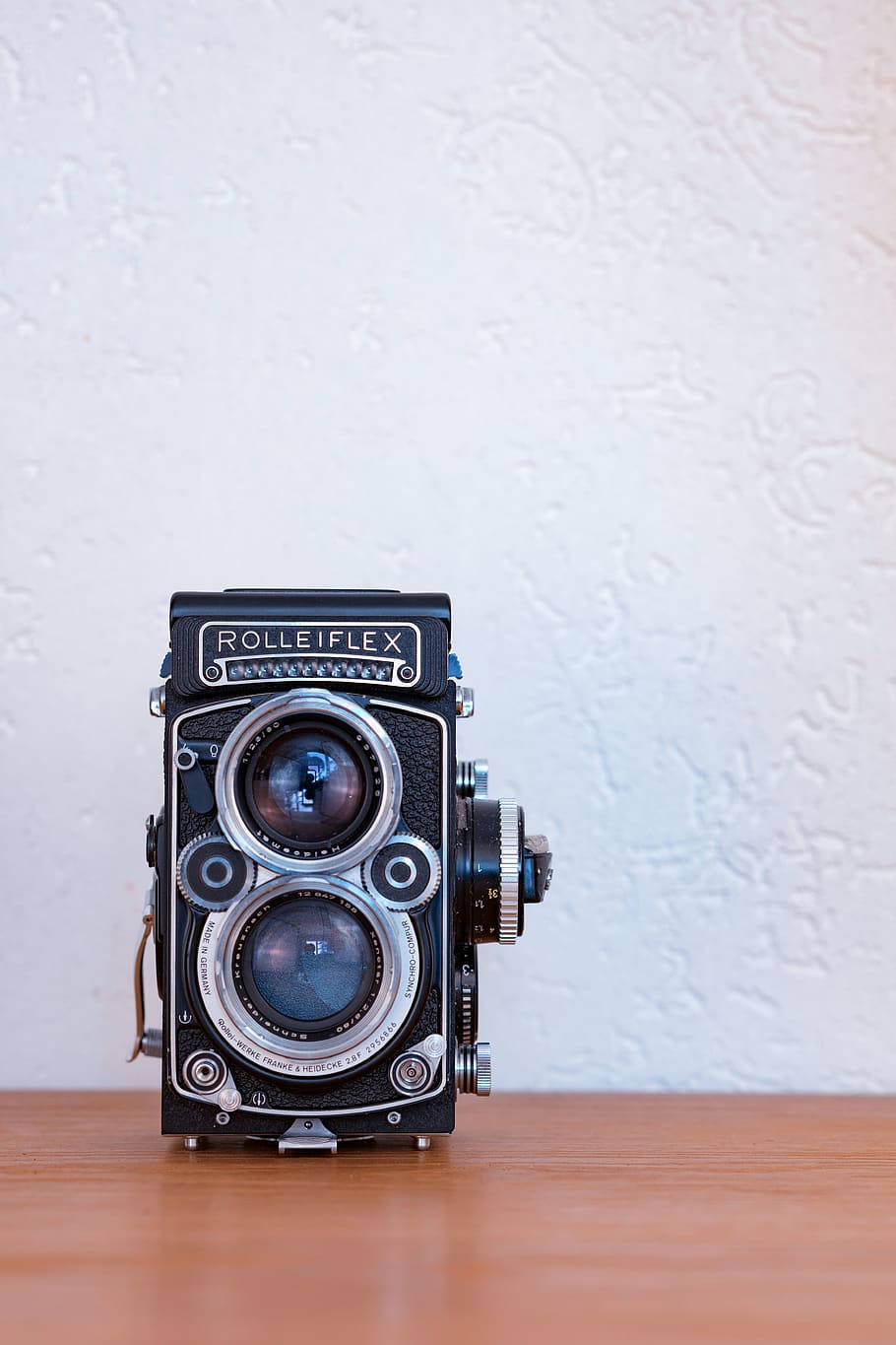 Vintage Minimalist 桌布 壁紙 — 一部經典 Rolleiflex 雙鏡反光相機居中放置在木質表面上，背景是帶紋理的白色牆壁。