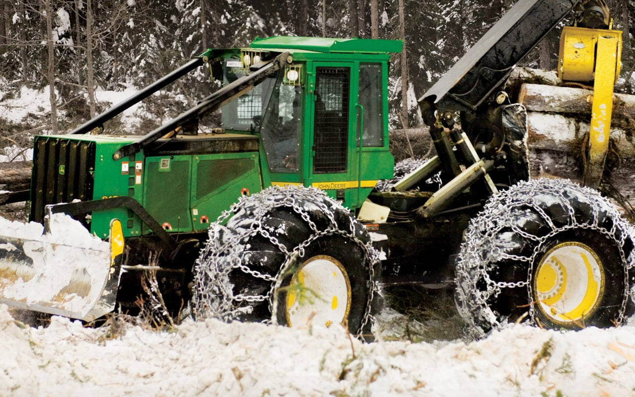 約翰迪爾 桌布 壁紙 — 一部綠色、配備雪地裝備的林業機器在積雪深厚的森林中行駛。