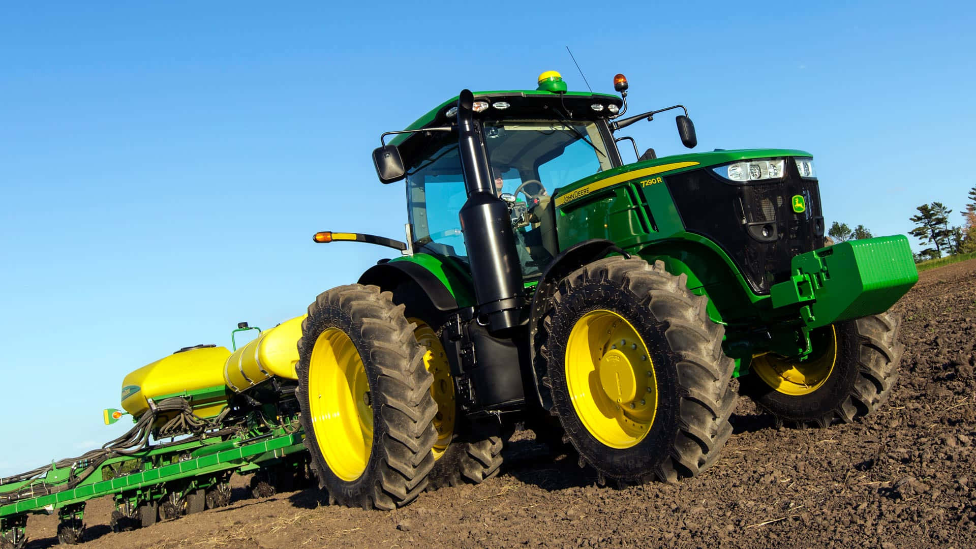 Tractor 桌布 壁紙 — 一部綠色和黃色的約翰迪爾拖拉機在晴朗的藍天下拖著播種機穿過深色耕作土壤。