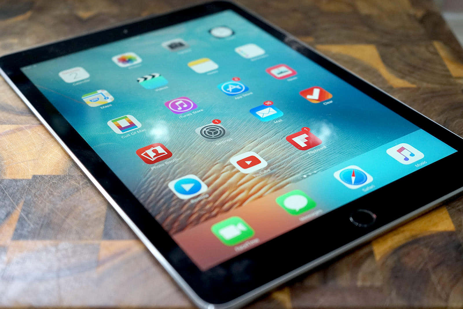 iPad 桌布 壁紙 — 一部纖薄的平板電腦顯示色彩繽紛的應用程式圖示，傾斜放置在帶有溫暖木紋圖案的木質表面上。