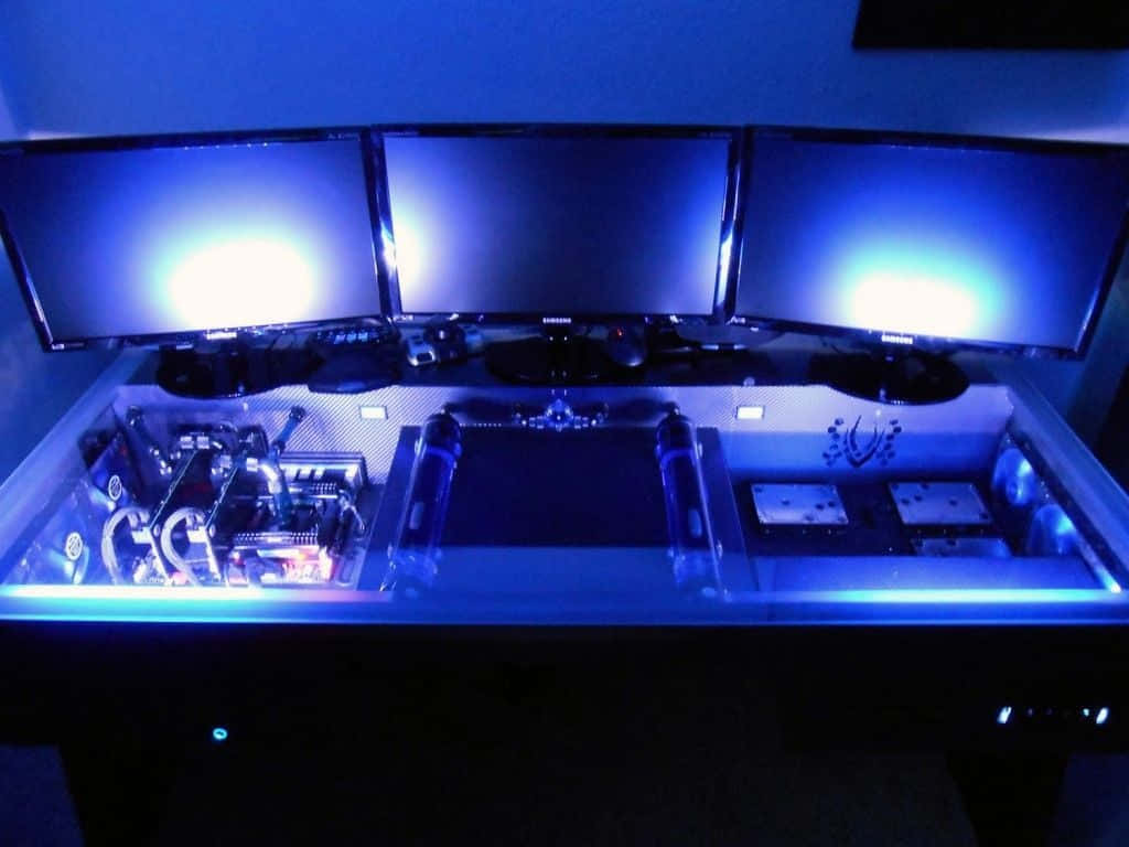 Gaming Pc 桌布 壁紙 — 一部自訂PC帶有發光藍色內部零件，放置於三台顯示器下方，處於昏暗的遊戲設置中。