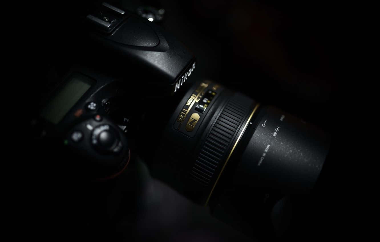 攝影 桌布 壁紙 — 一部配備金環鏡頭的 Nikon DSLR 相機在近乎黑暗中微微發光，突顯其紋理控制和專業構造。