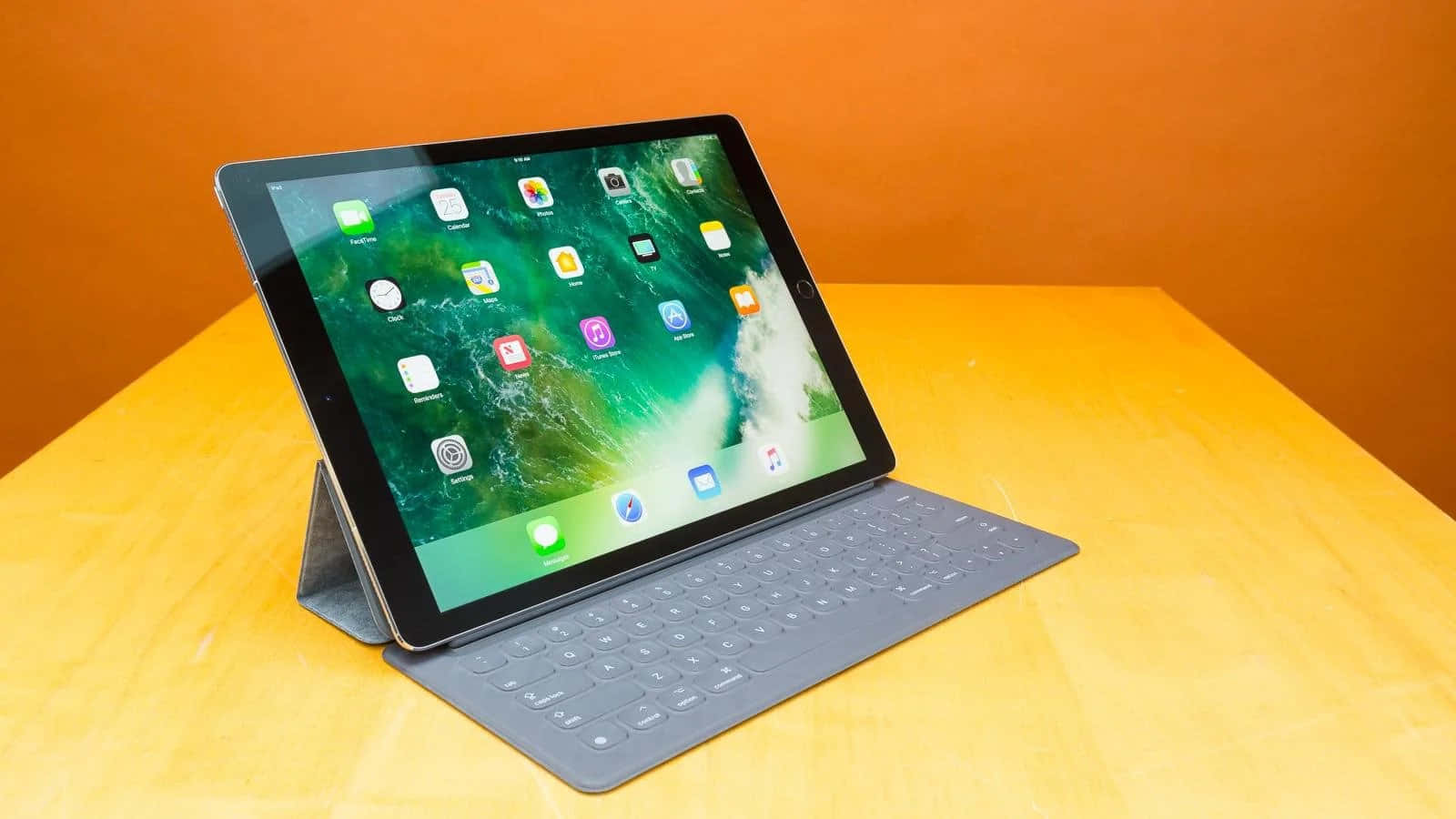 iPad 桌布 壁紙 — 一部配備鍵盤保護套的時尚平板電腦放在木桌上，背景是溫暖的橙色牆壁。