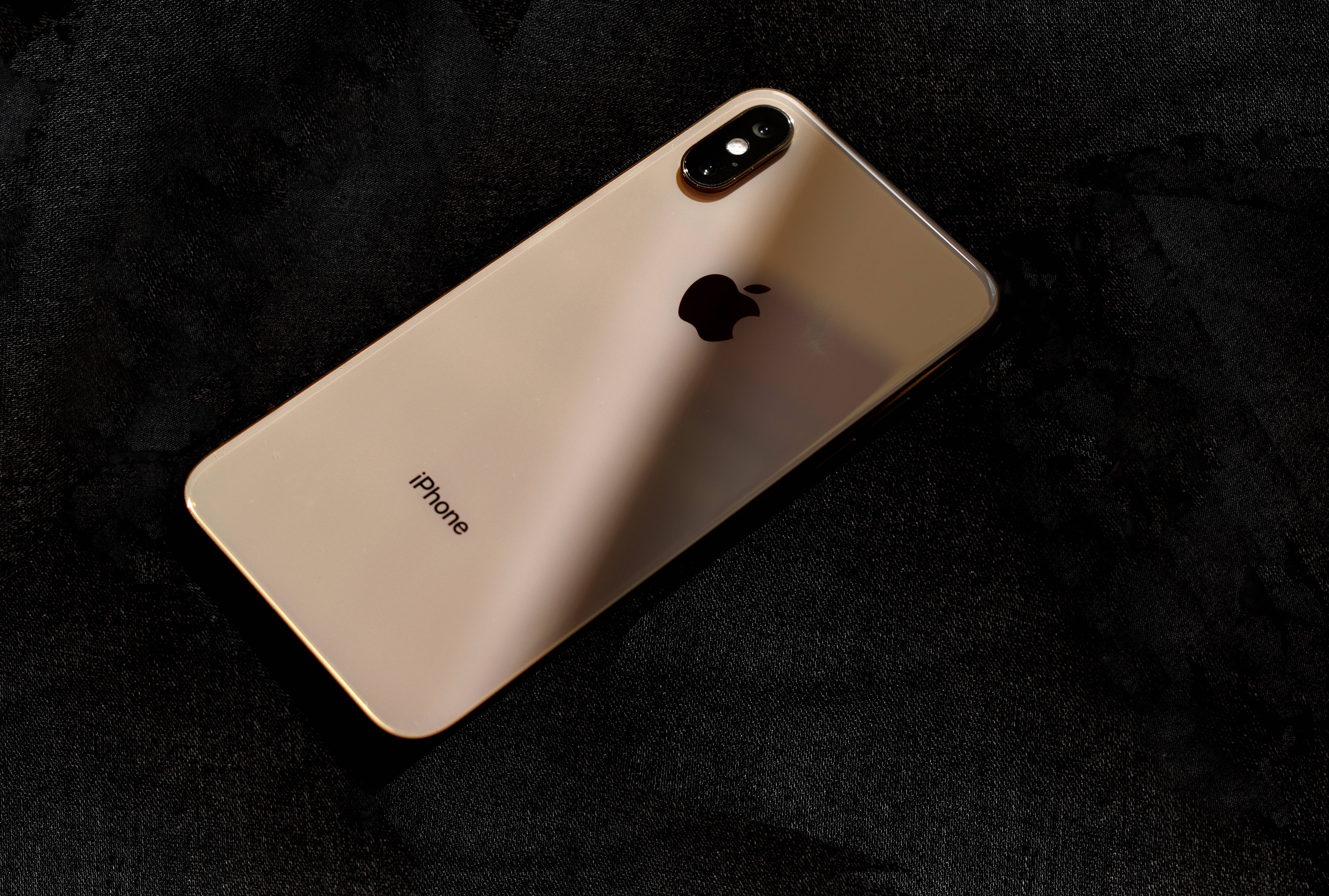 iPhone 桌布 壁紙 — 一部金色iPhone X在柔和定向燈光下，對角放置在帶有紋理的黑色布料表面上。