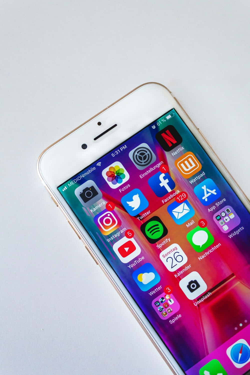 Application 桌布 壁紙 — 一部金色iPhone，螢幕上顯示色彩繽紛的應用程式網格，對角放置在純白色表面上。