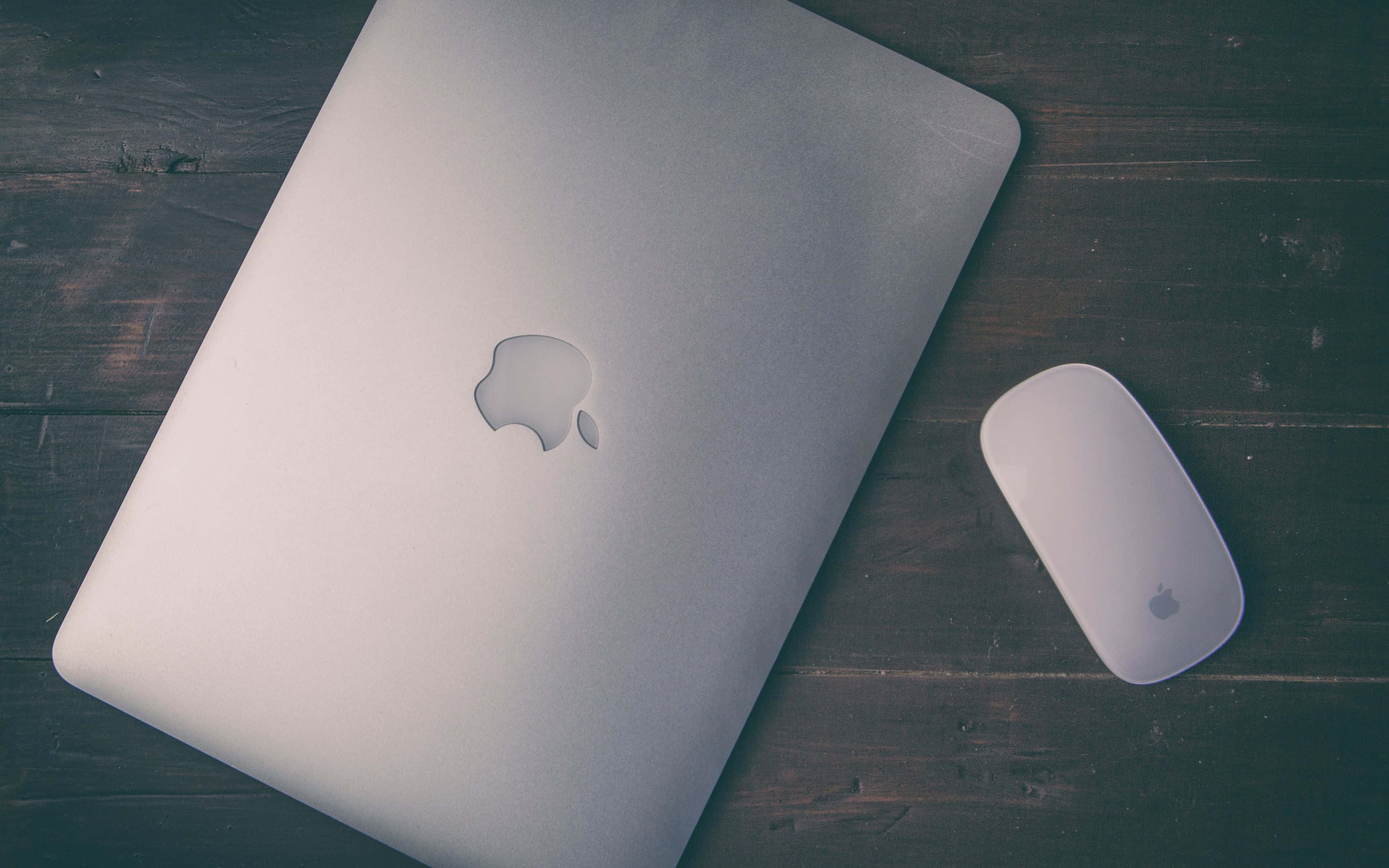 桌布 壁紙 — 一部銀色 MacBook 和相配的滑鼠放在色調柔和的深色鄉村風格木桌上。