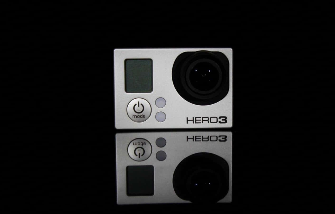 gopro 桌布 壁紙 — 一部銀色GoPro HERO3相機居中放置在反光的黑色表面上，其倒影映照出其時尚設計。