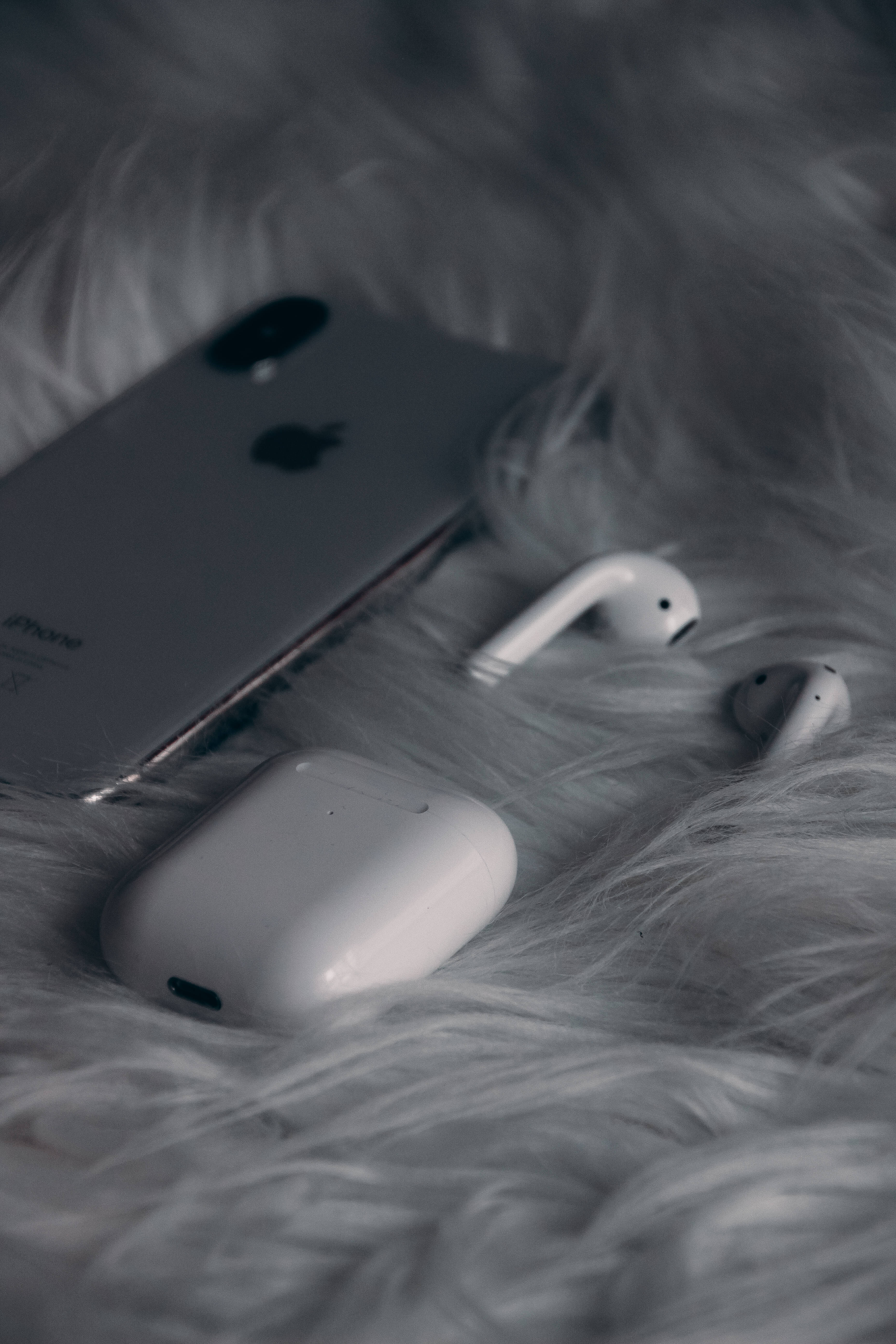 Love iPhone 桌布 壁紙 — 一部銀色iPhone和白色AirPods保護殼放在柔軟蓬鬆的灰色地毯上，呈現極簡主義單色佈置。