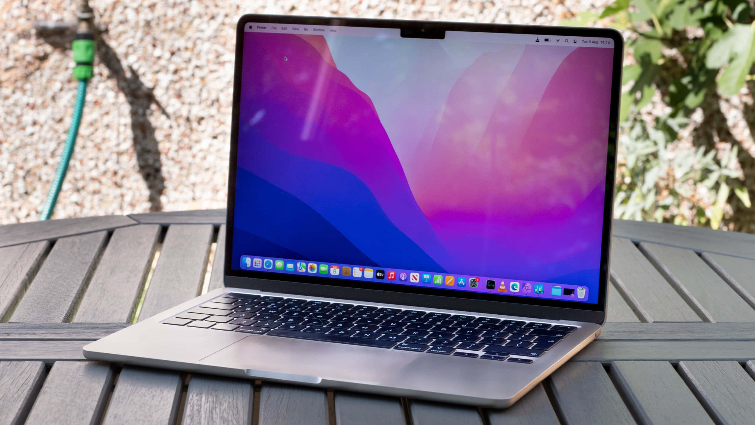 MacBook 動態圖片 桌布 壁紙 — 一部銀色筆記型電腦，帶有充滿活力的紫色和藍色抽象桌布，打開放在戶外的木條桌上。