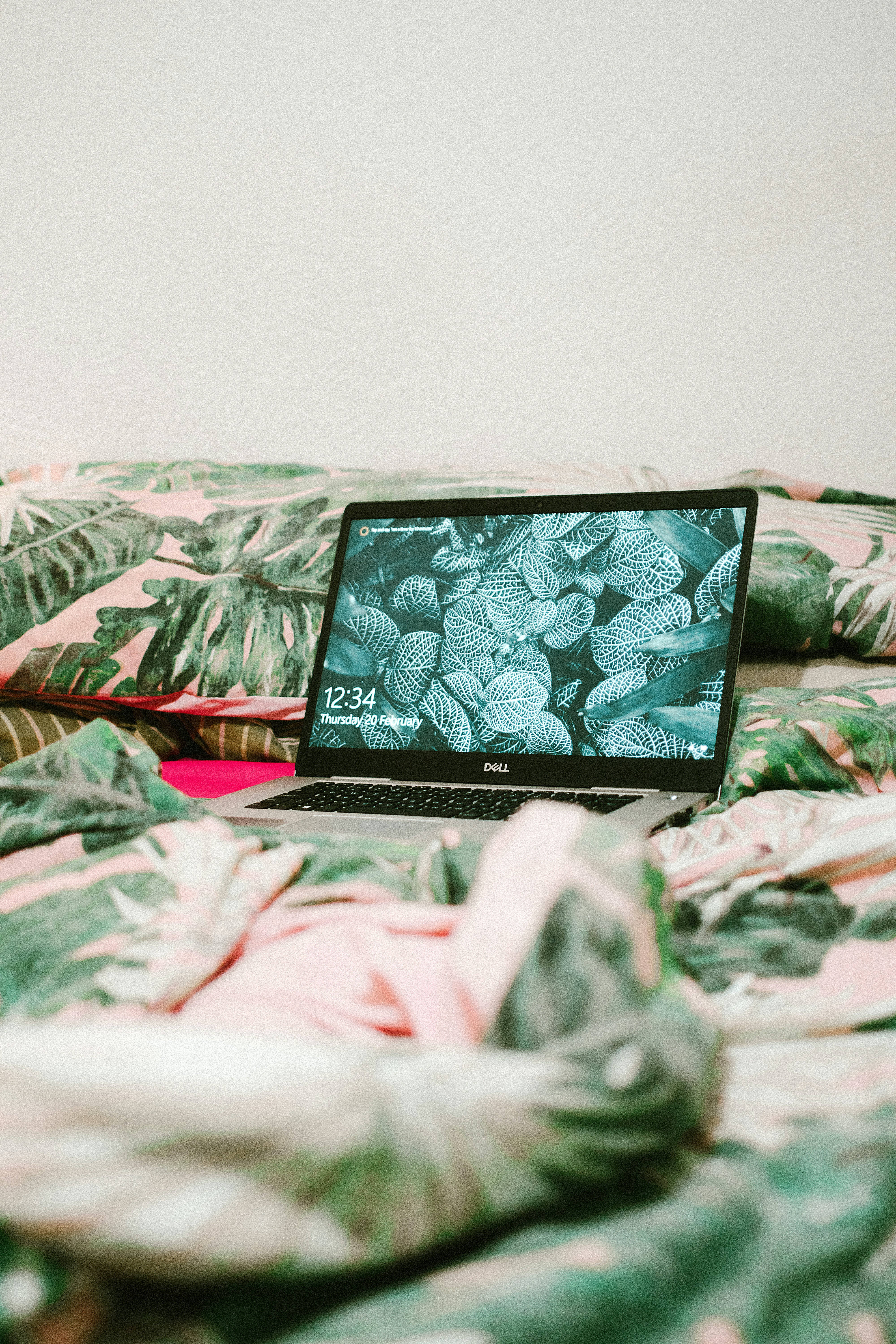 Cute Laptop 桌布 壁紙 — 一部銀色筆記型電腦放在一張皺巴巴的粉紅和綠色葉紋床罩上，背景是純白牆壁。