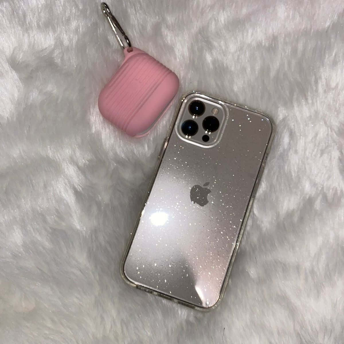 iPhone 12 桌布 壁紙 — 一部銀色閃粉iPhone和粉紅色AirPods保護殼放在毛絨白色紋理表面上。