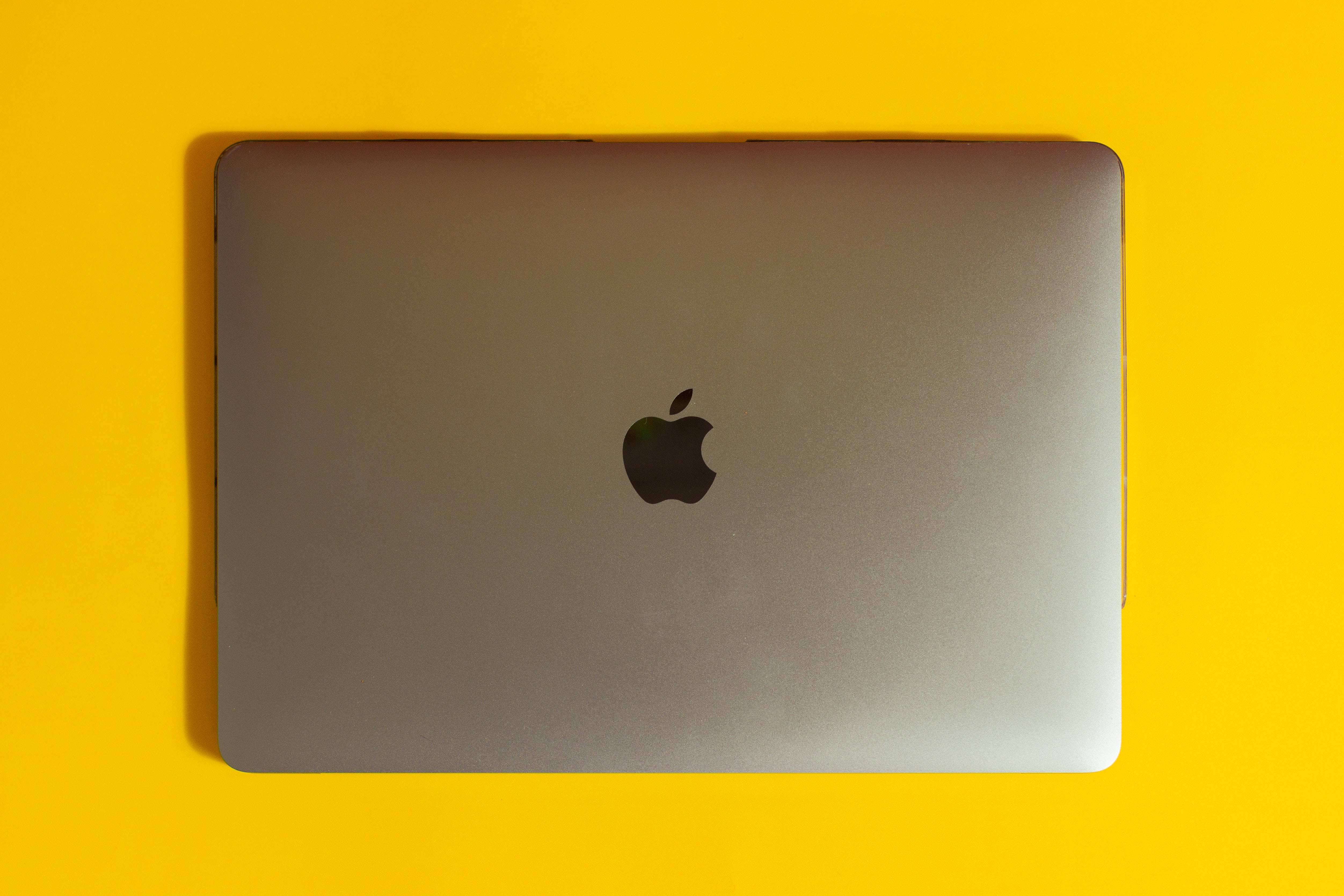 Mac 桌布 壁紙 — 一部關閉的銀色 MacBook 筆記型電腦，置於鮮黃色背景中央，帶有柔和陰影。