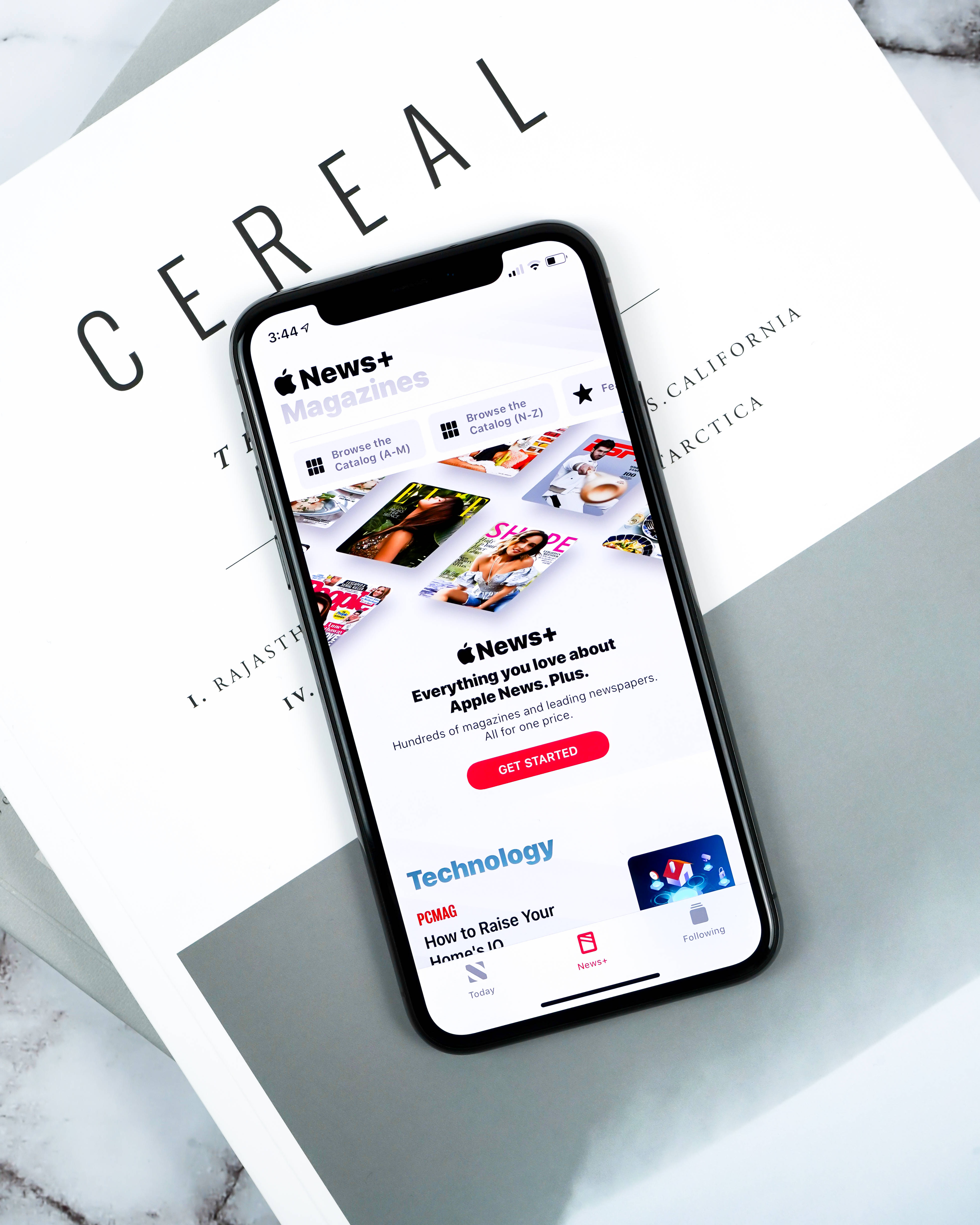 iPhone 桌布 壁紙 — 一部顯示 Apple News+ 雜誌應用程式的智慧型手機，放在一個白色書本 'CEREAL' 上，書本置於大理石表面。