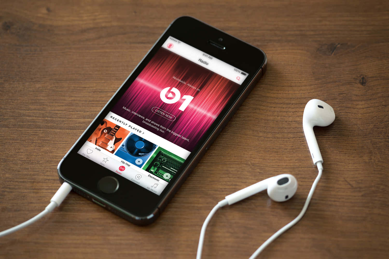 Apple Phone 桌布 壁紙 — 一部顯示 Beats 1 收音機應用程式的智慧型手機放在木桌上，旁邊有白色有線耳機。