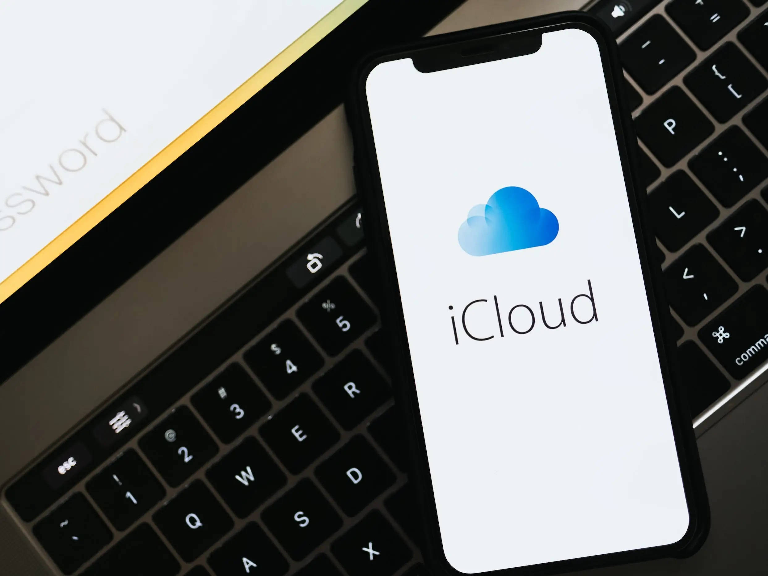 Internet 桌布 壁紙 — 一部顯示 iCloud 標誌的智慧型手機放在黑色鍵盤上，旁邊有一張密碼卡。