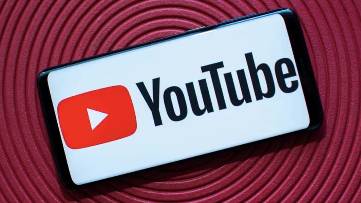 YouTube 桌布 壁紙 — 一部顯示 YouTube 標誌的智慧型手機放置在帶紋理的紅色螺旋表面上。