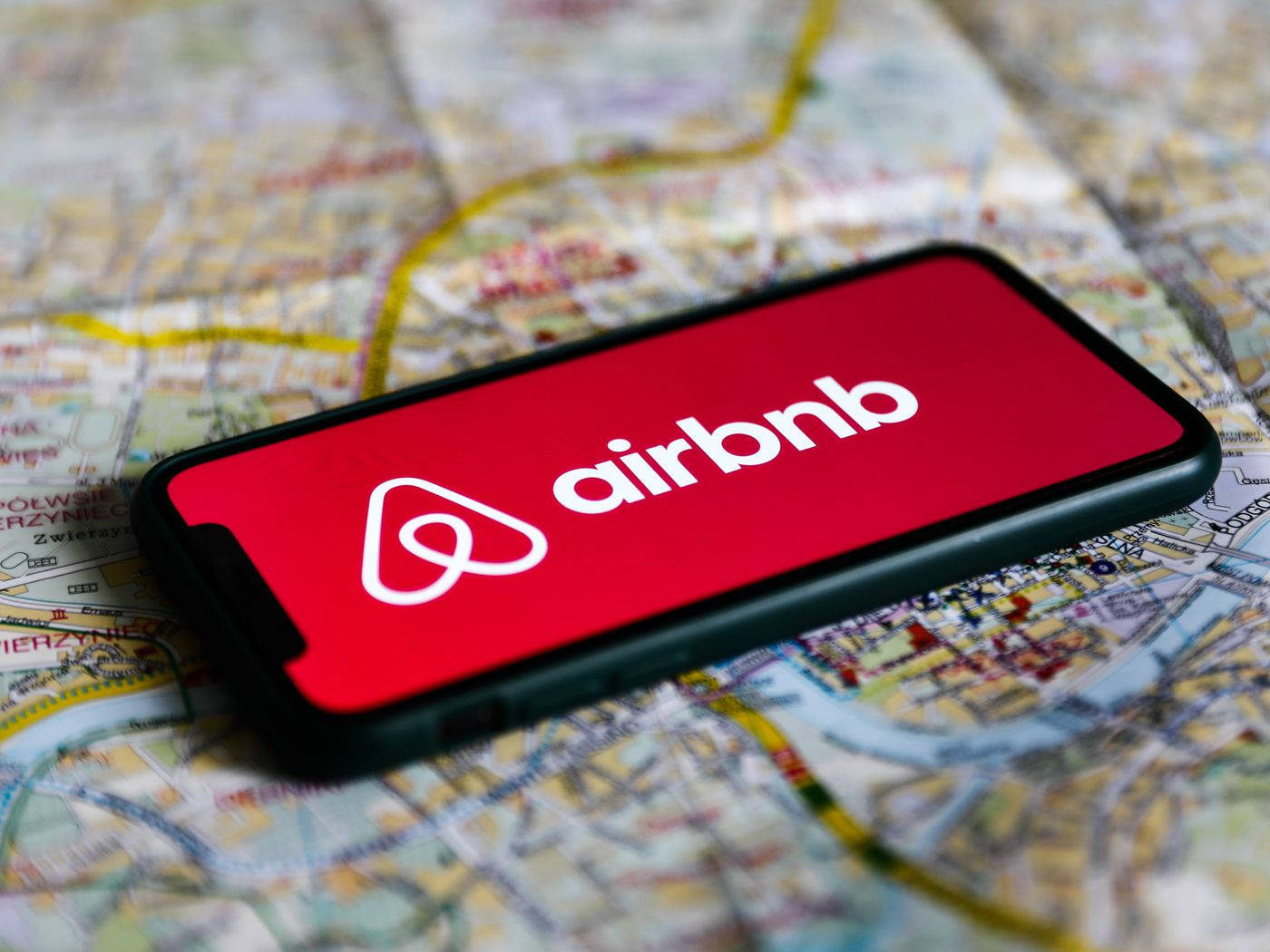 標誌 桌布 壁紙 — 一部顯示Airbnb標誌的智慧型手機放在詳細的城市地圖上，暗示旅行和住宿預訂。