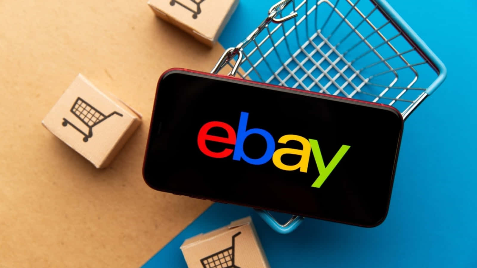 eBay 桌布 壁紙 — 一部顯示eBay標誌的智慧型手機放在一個微型購物車內，周圍是帶有購物車圖標的紙箱。