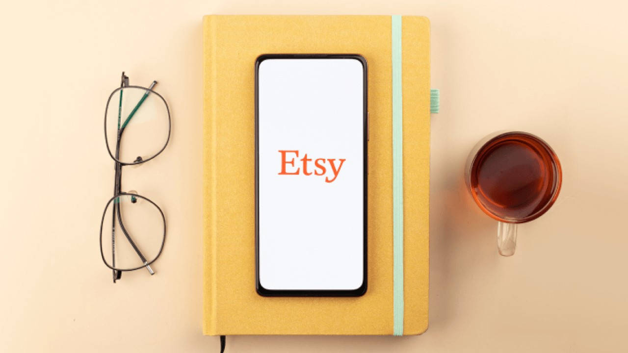 etsy 桌布 壁紙 — 一部顯示Etsy的智慧型手機放在黃色筆記本上，旁邊有眼鏡和一杯茶，極簡風格的平鋪構圖。